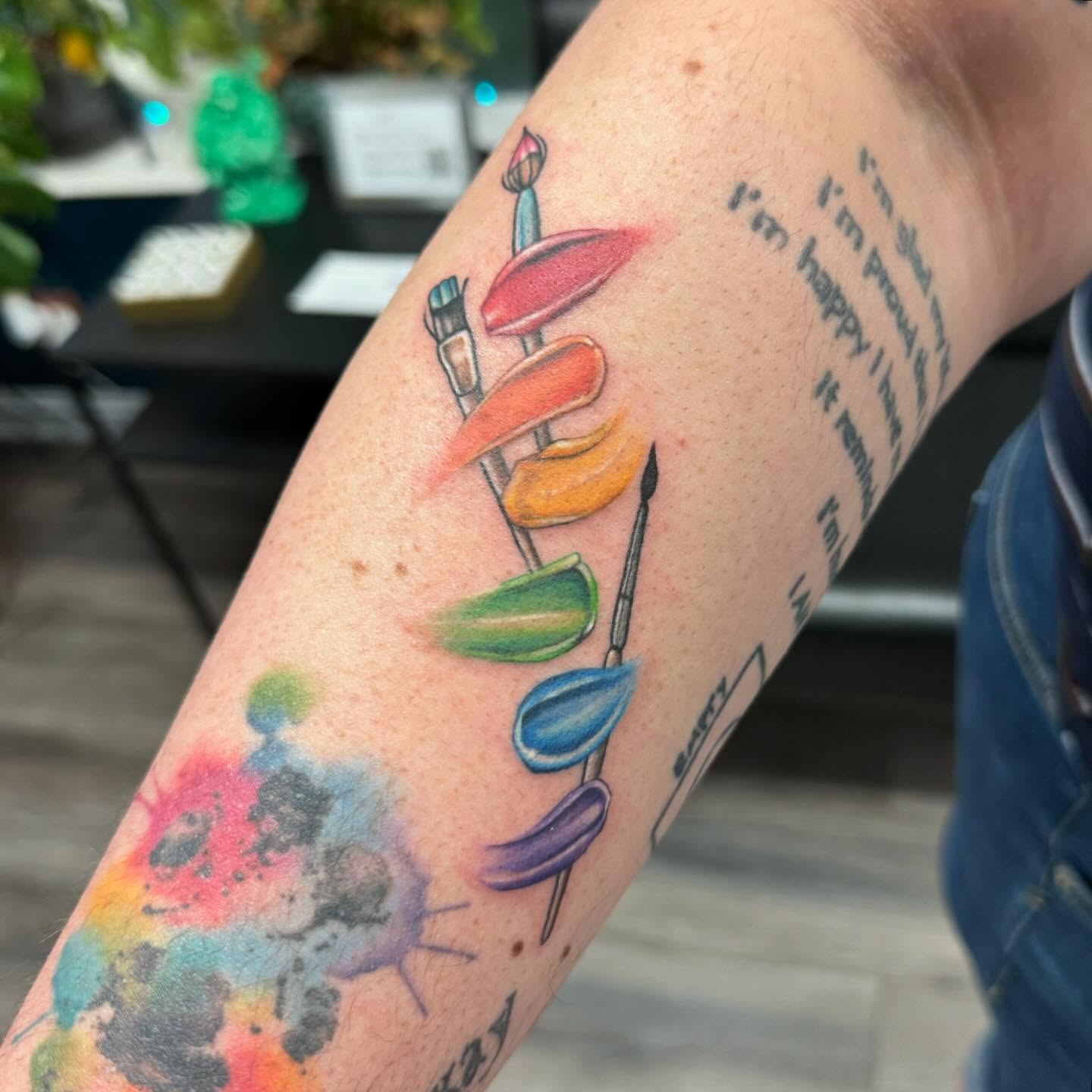 Paintbrushes and paint palettes watercolor tattoo on the forearm by Robyn Mahon