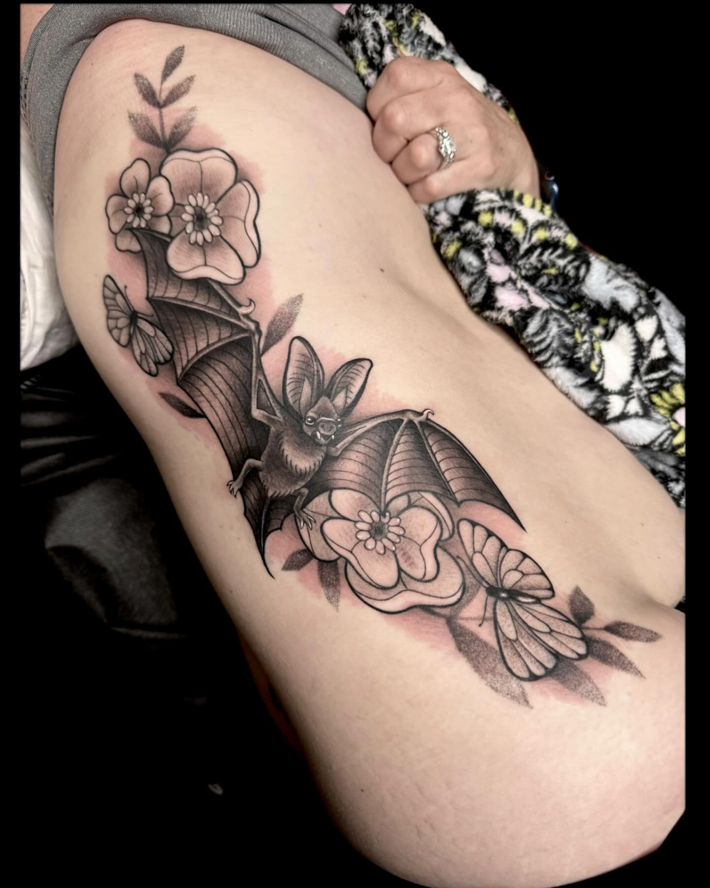 Bat and flowers black and grey tattoo on the thigh by Amber