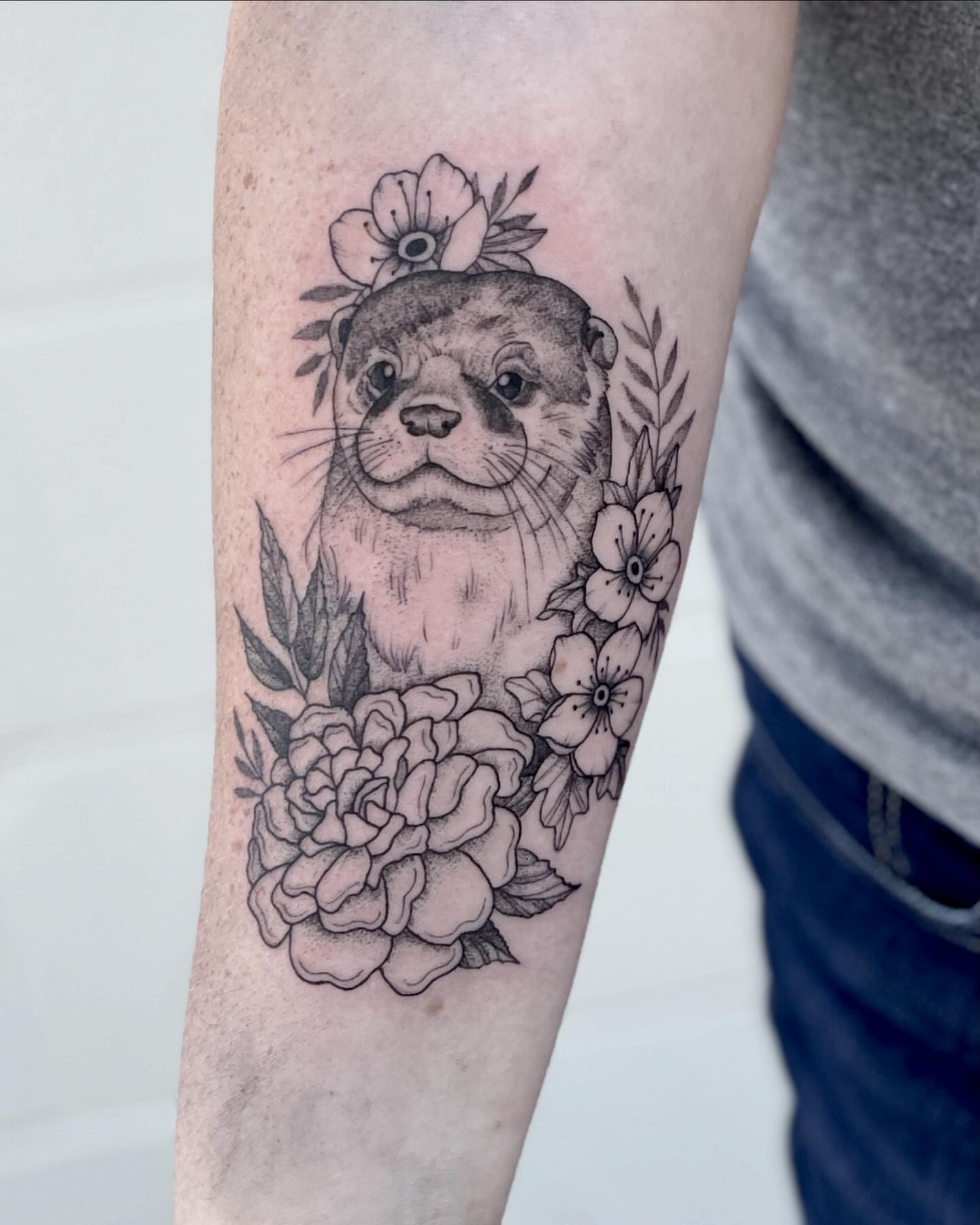 Otter with flowers black and grey tattoo on the forearm by Katie Stacy