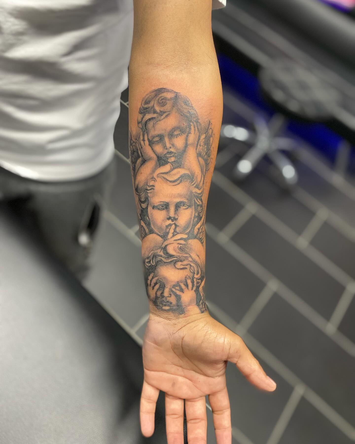 Three-headed cherub black and grey tattoo on the forearm by Chino's Tattoos