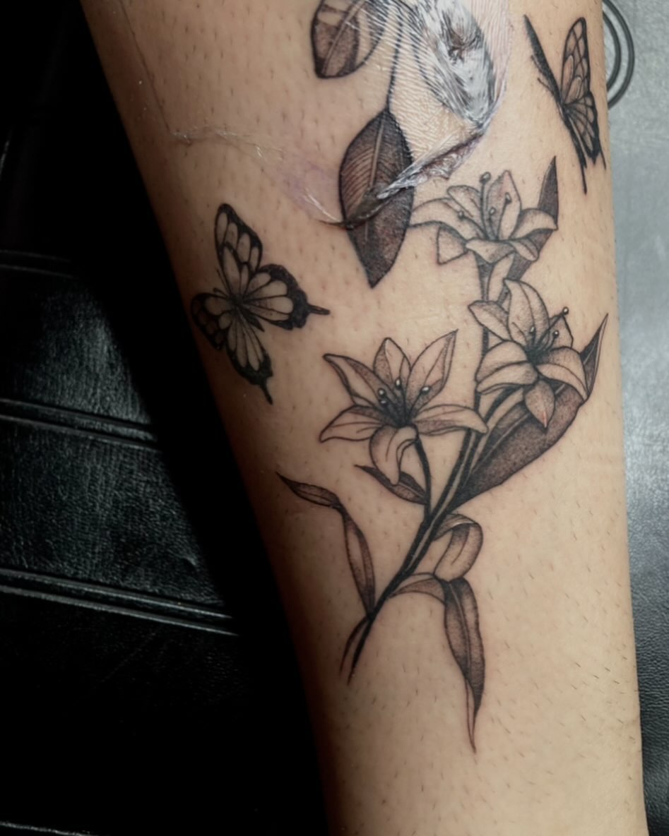Lilies and butterflies black and grey tattoo on the forearm by V
