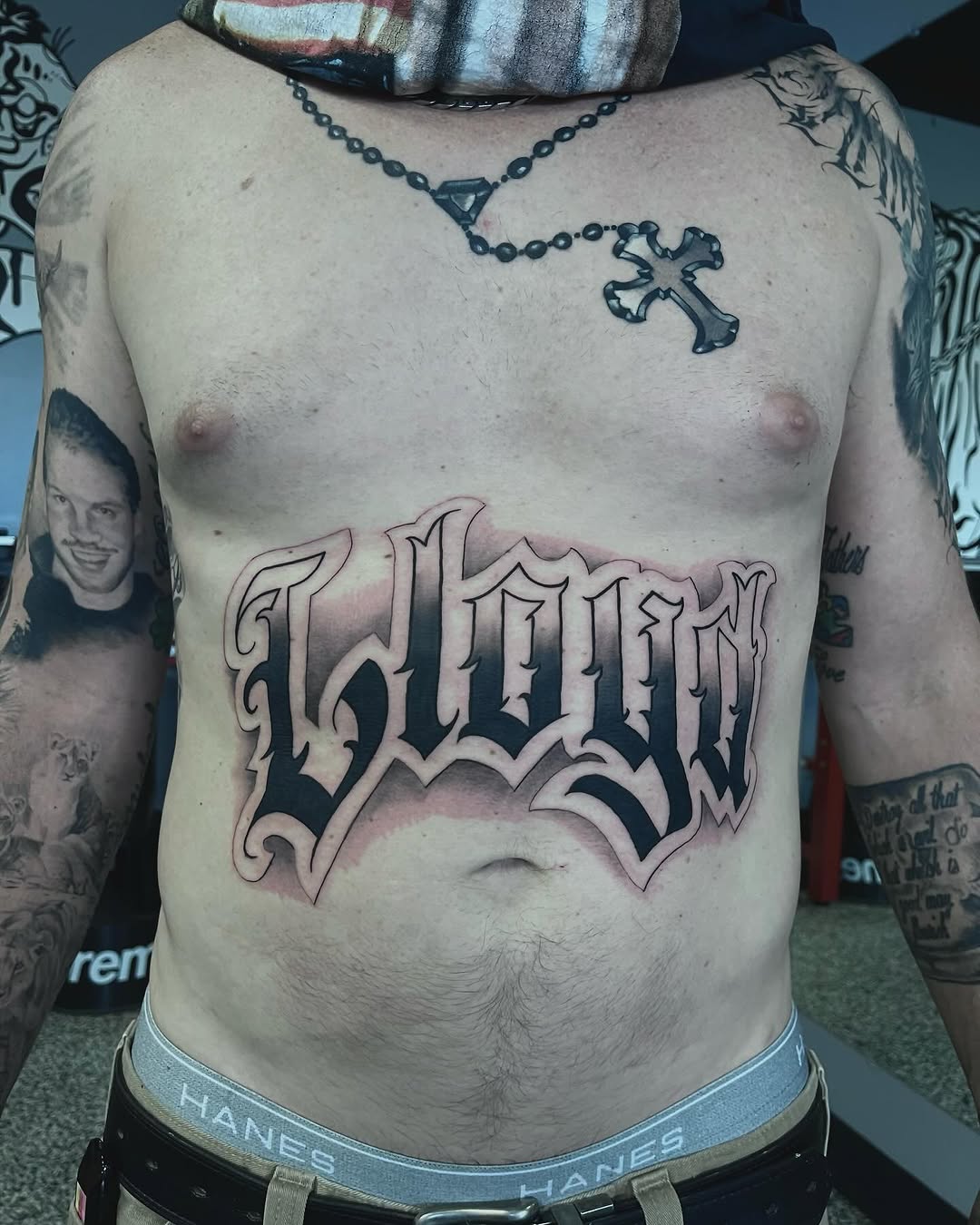 Script lettering Chicano tattoo on the chest by Jonathan Red