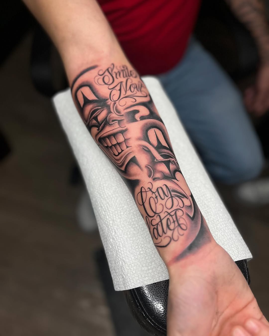Comedy and tragedy masks with script realism tattoo on the forearm by Tattoo Artist
