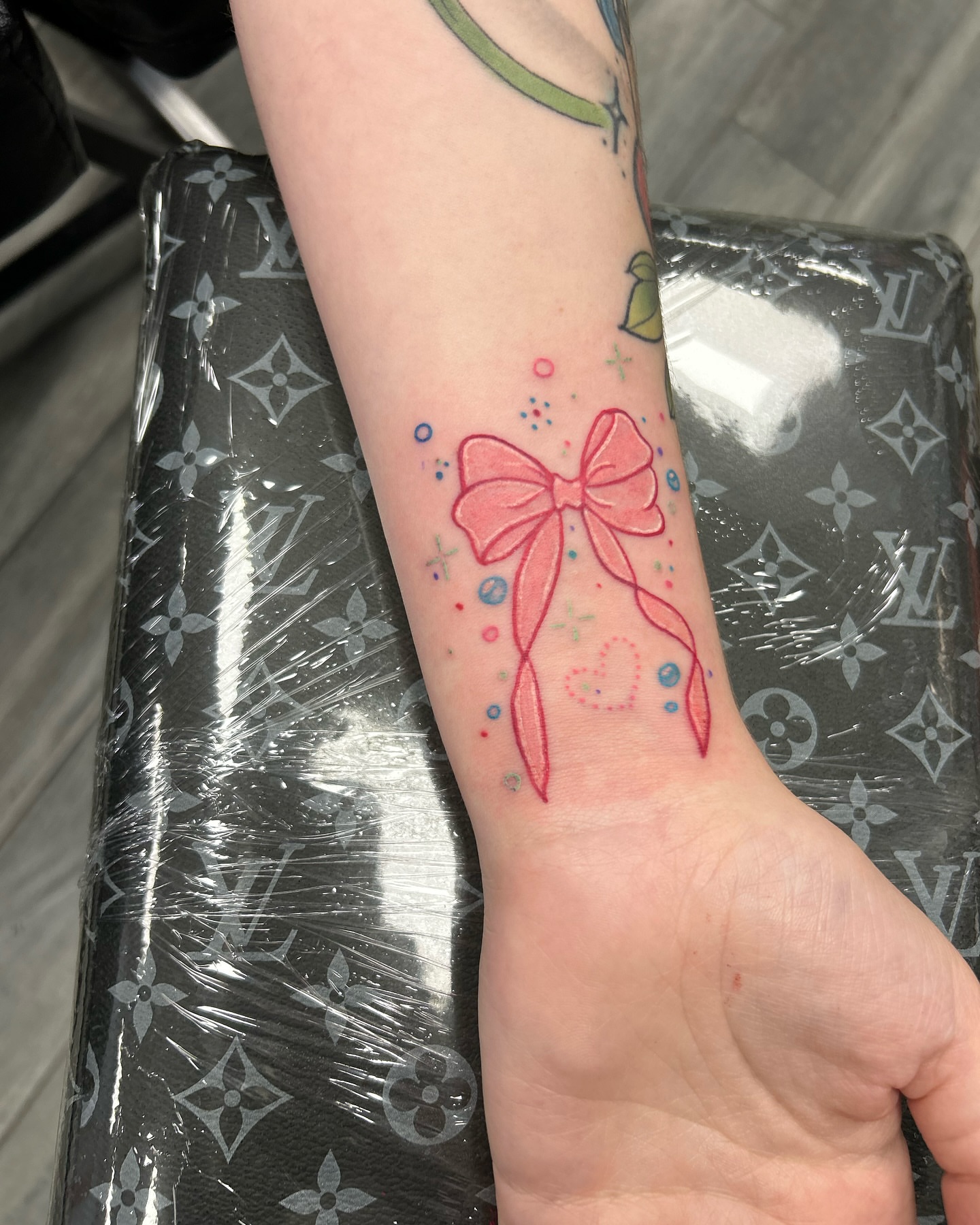 Bow watercolor tattoo on the forearm by Brittany Brutal
