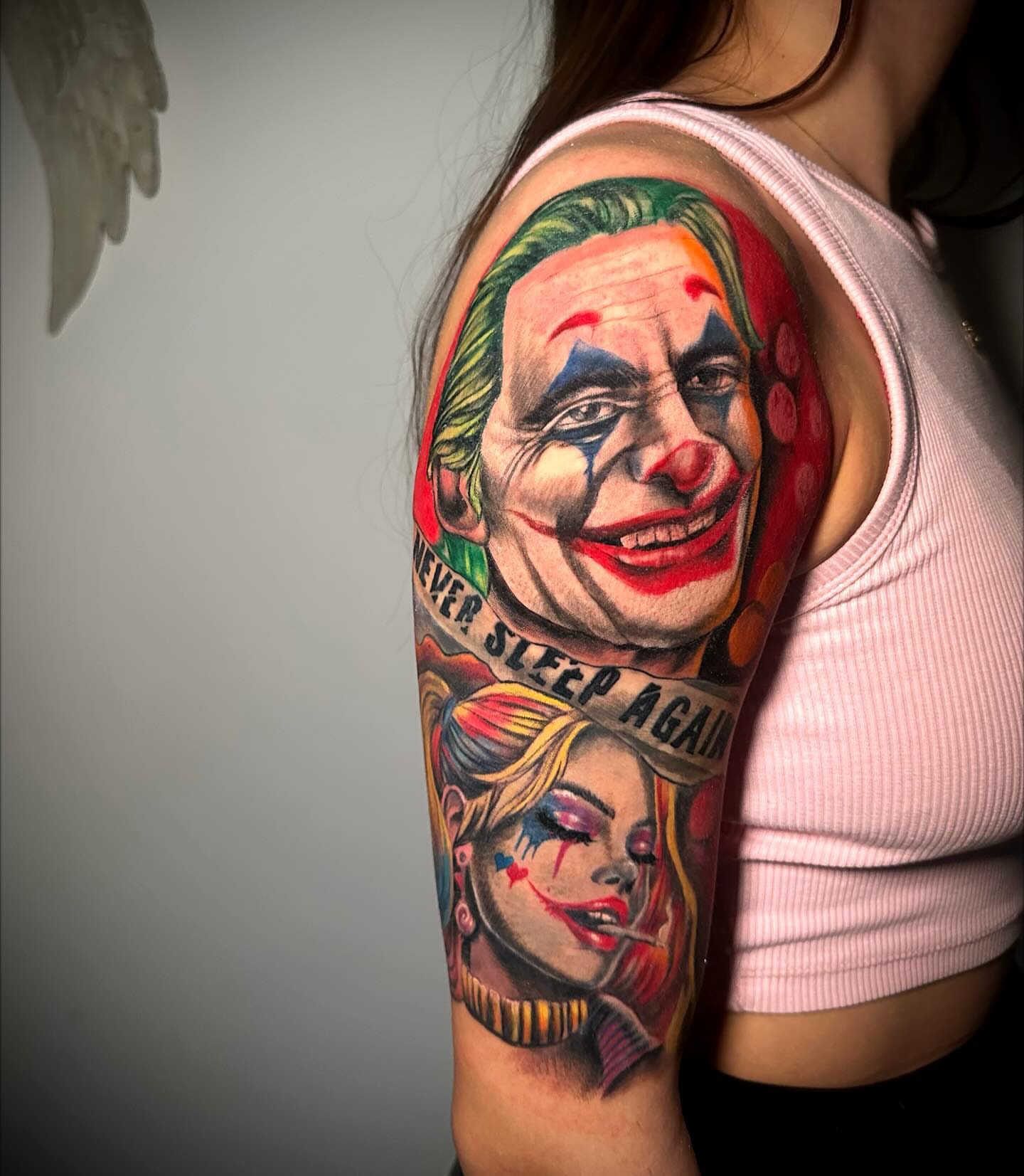 Joker and woman realism tattoo on the upper arm by Anghel Patricia