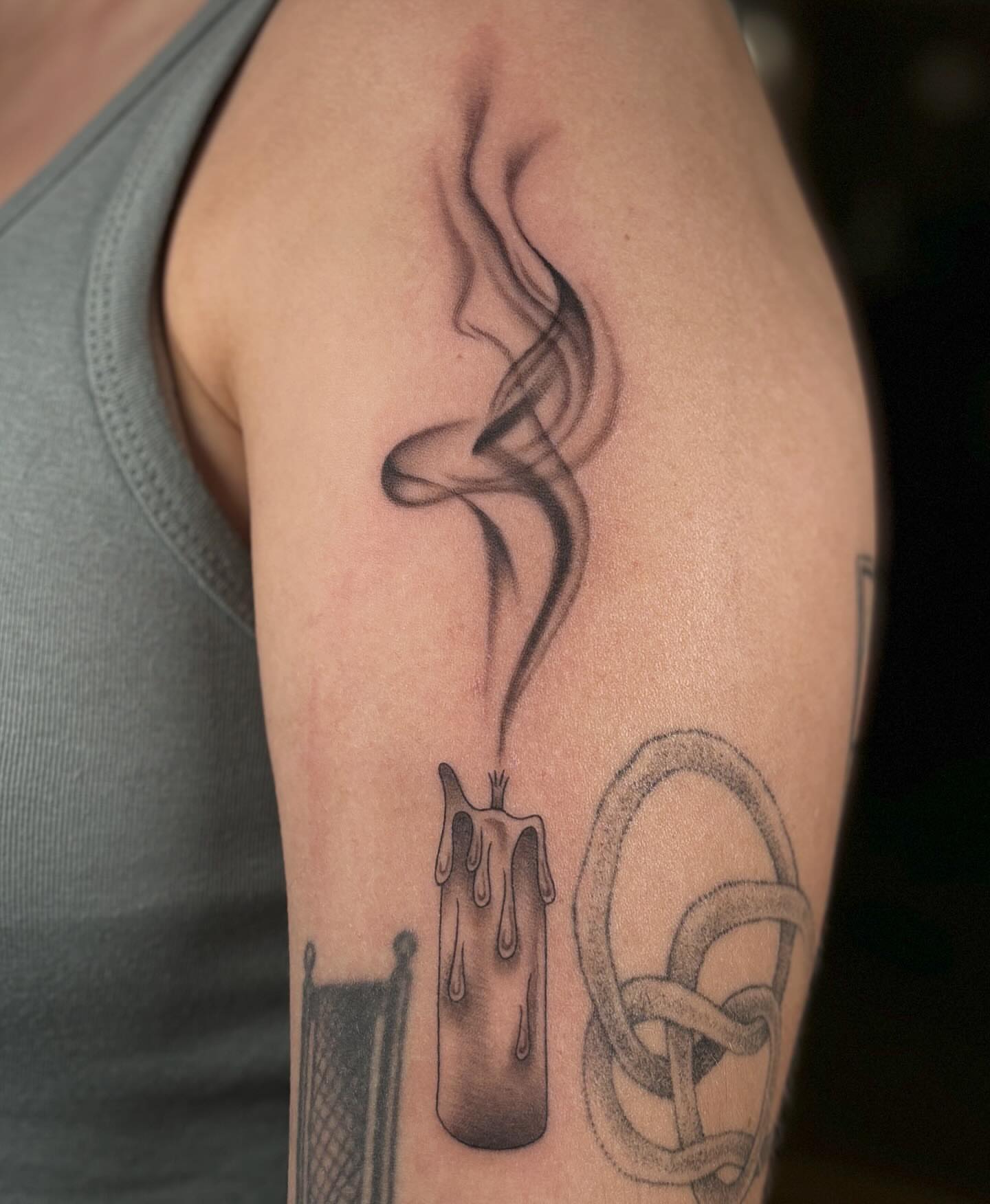 Smoking candle black and grey tattoo on the upper arm by Anna Sage