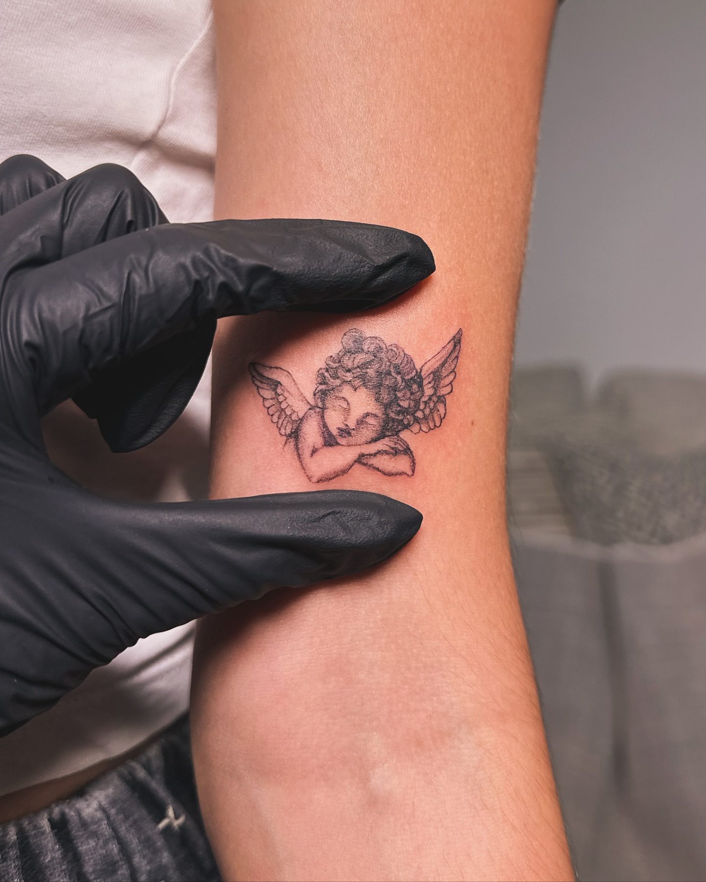 Cherub black and grey tattoo on the forearm by Katherin Plaza