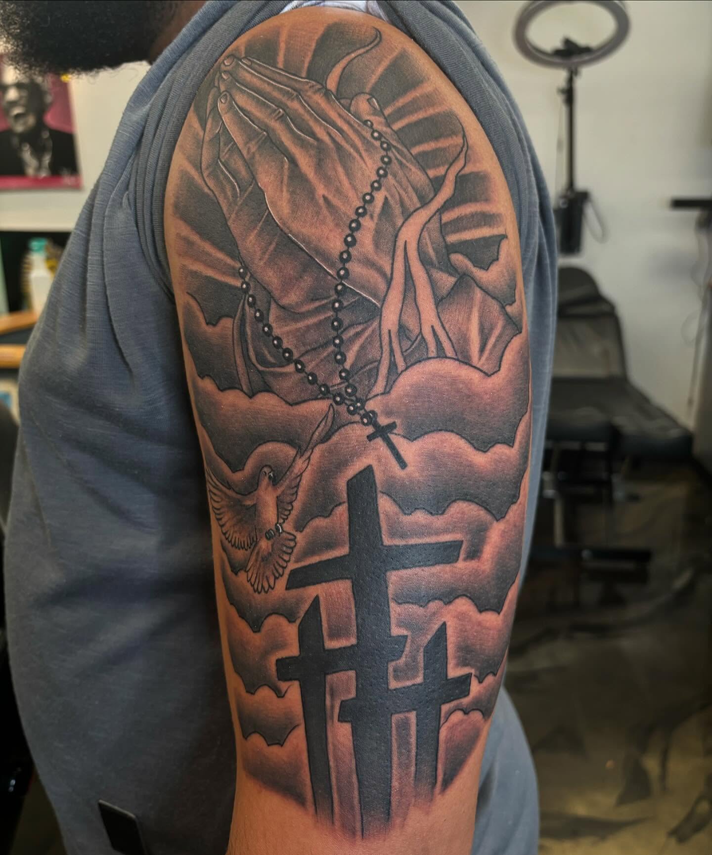 Praying hands with rosary realism tattoo on the upper arm by Tattoos By Rico