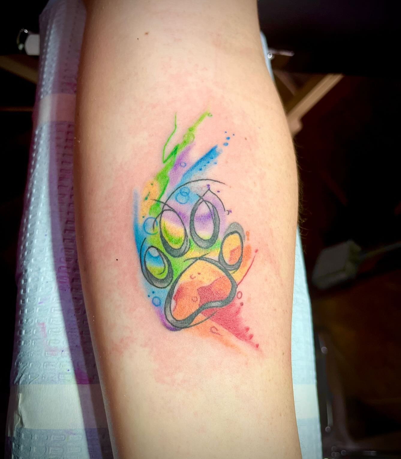 Rainbow paw print watercolor tattoo on the forearm by Kenny Buck