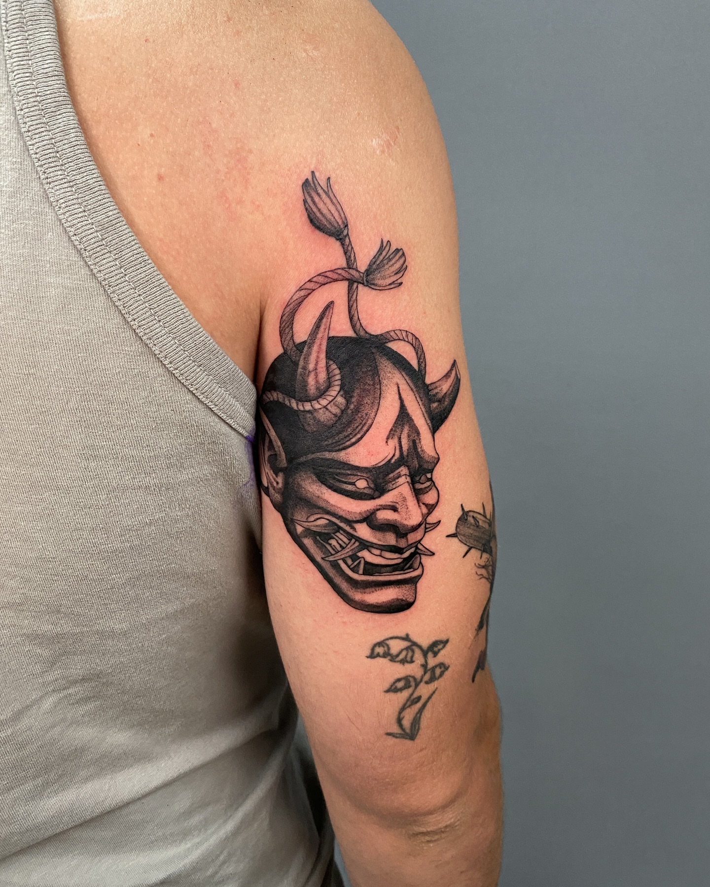 Demon mask black and grey tattoo on the upper arm by Tattoo Artist