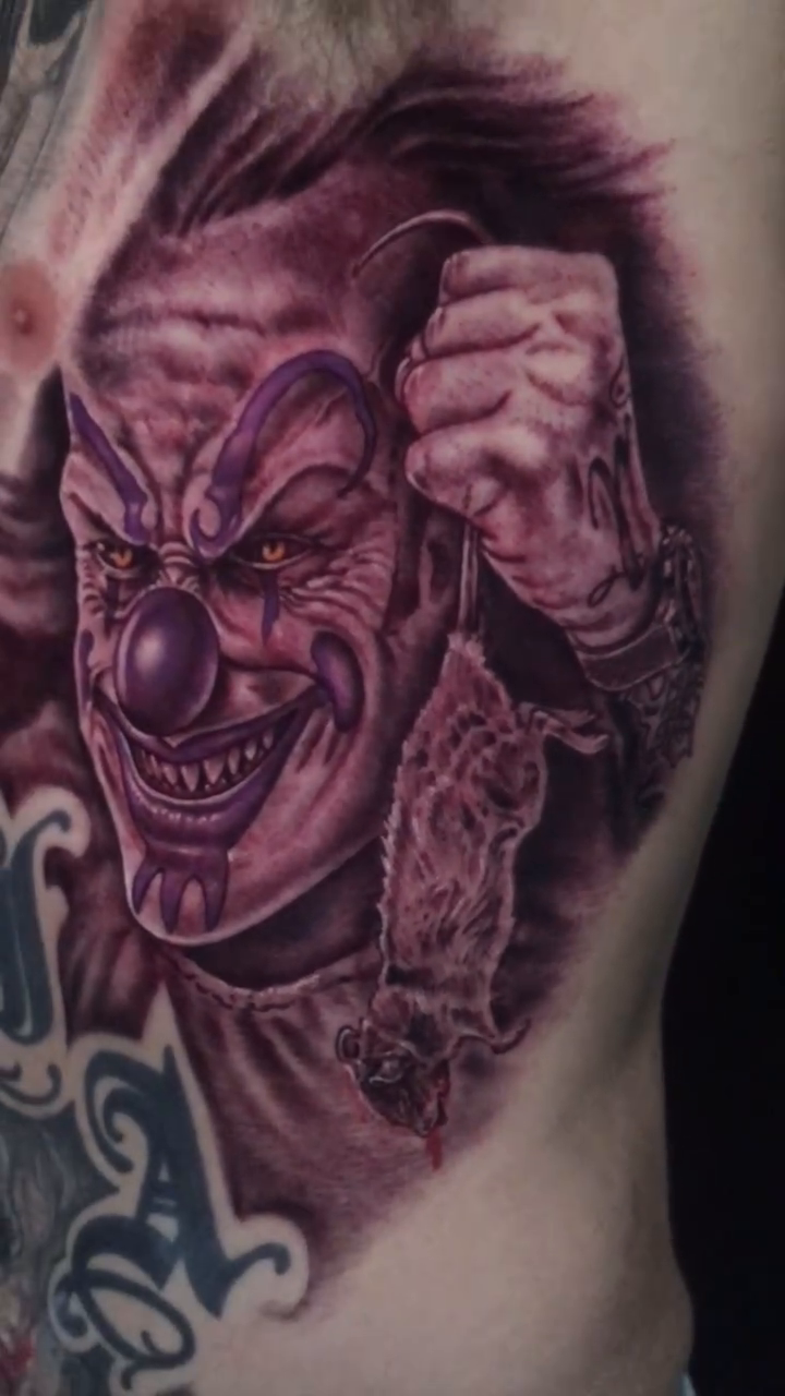 Evil clown holding a rat realism tattoo by Jose Calderon