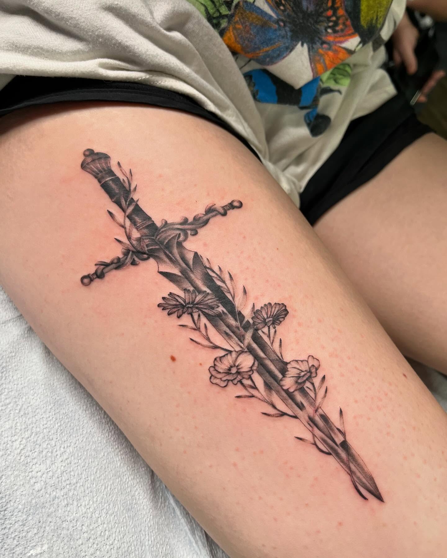Sword and flowers realism tattoo on the thigh by jude tattoos