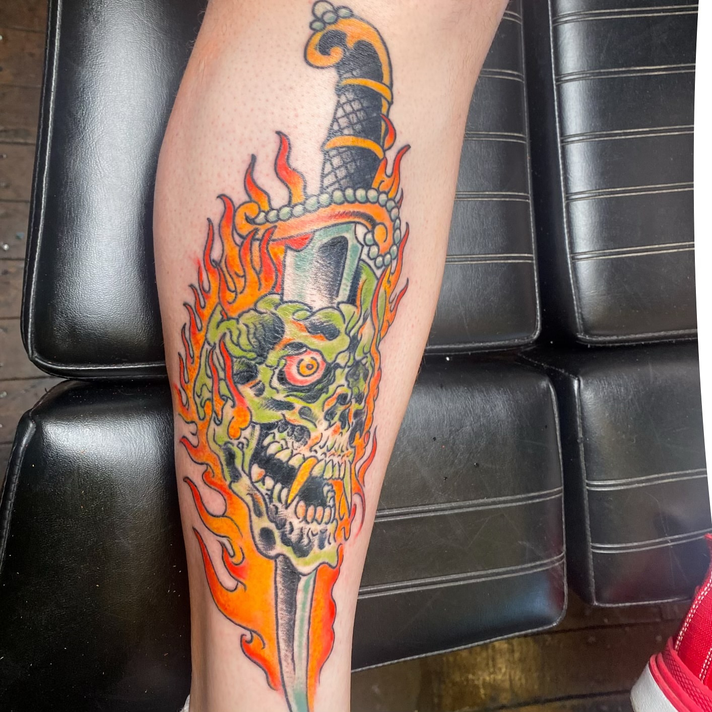 Flaming skull with sword American traditional tattoo on the leg by Benjamin Carlson