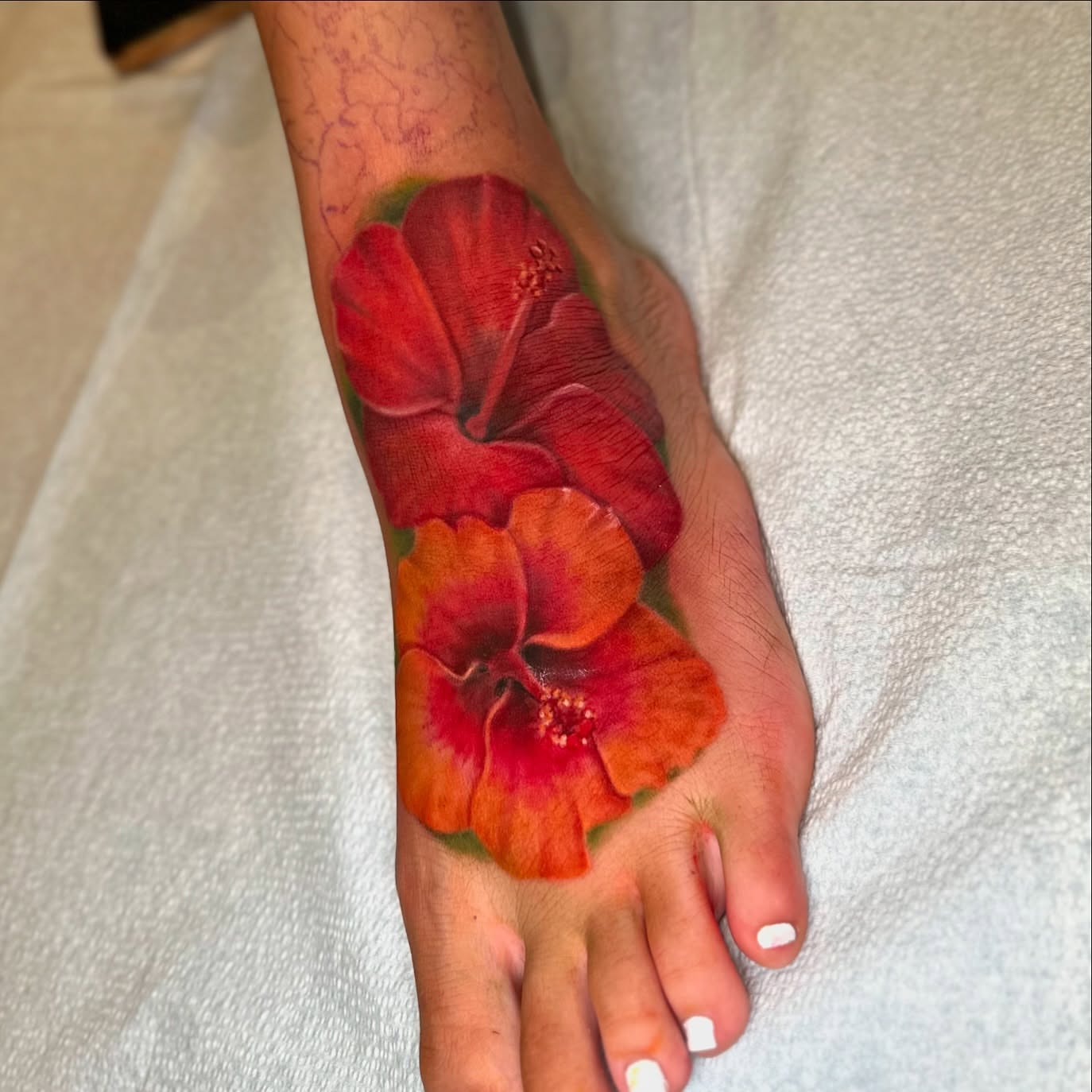 Red hibiscus flowers realism tattoo on the foot by Junior Nunez