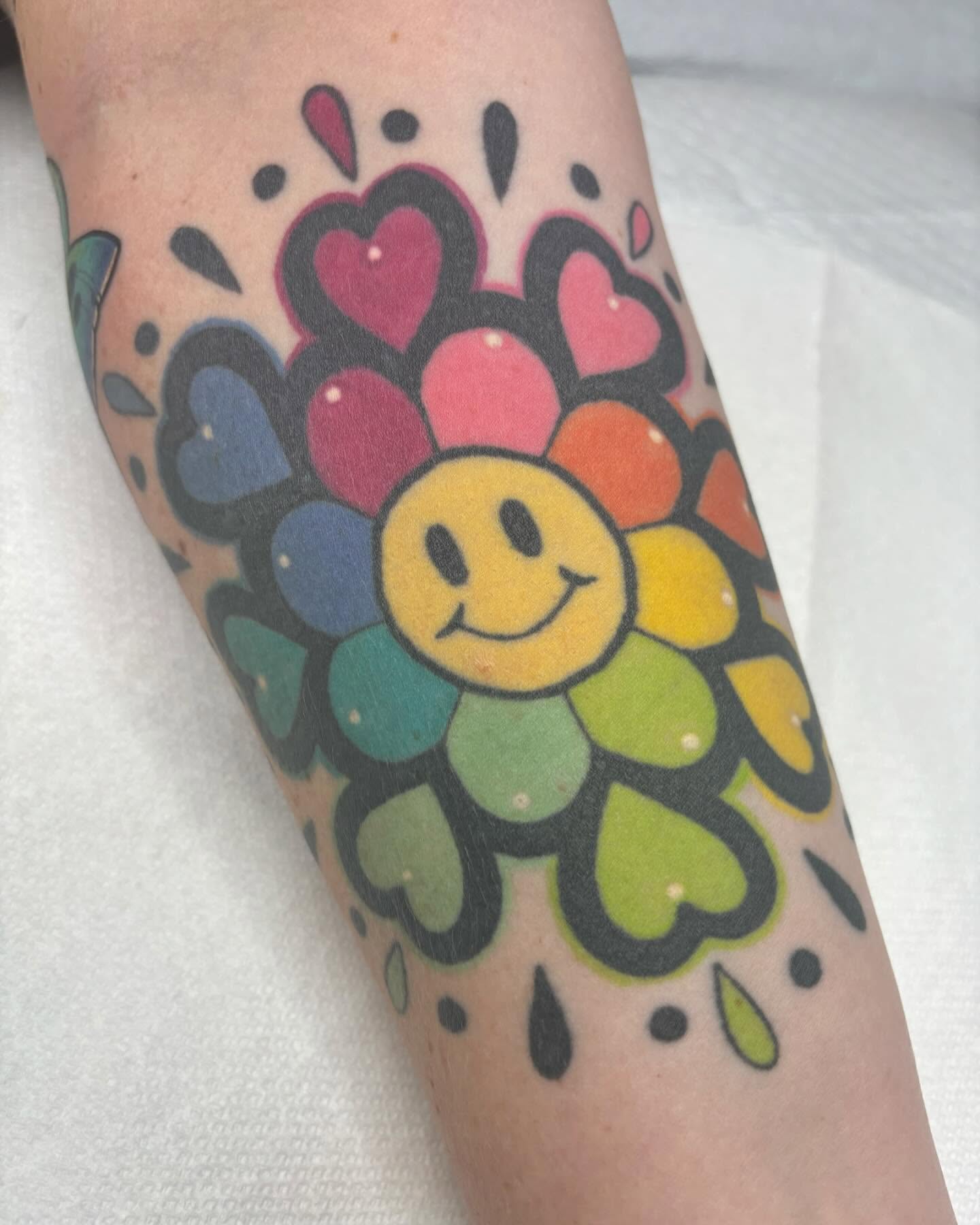 Flower with smiley face new school tattoo on the forearm by Carly Zehring