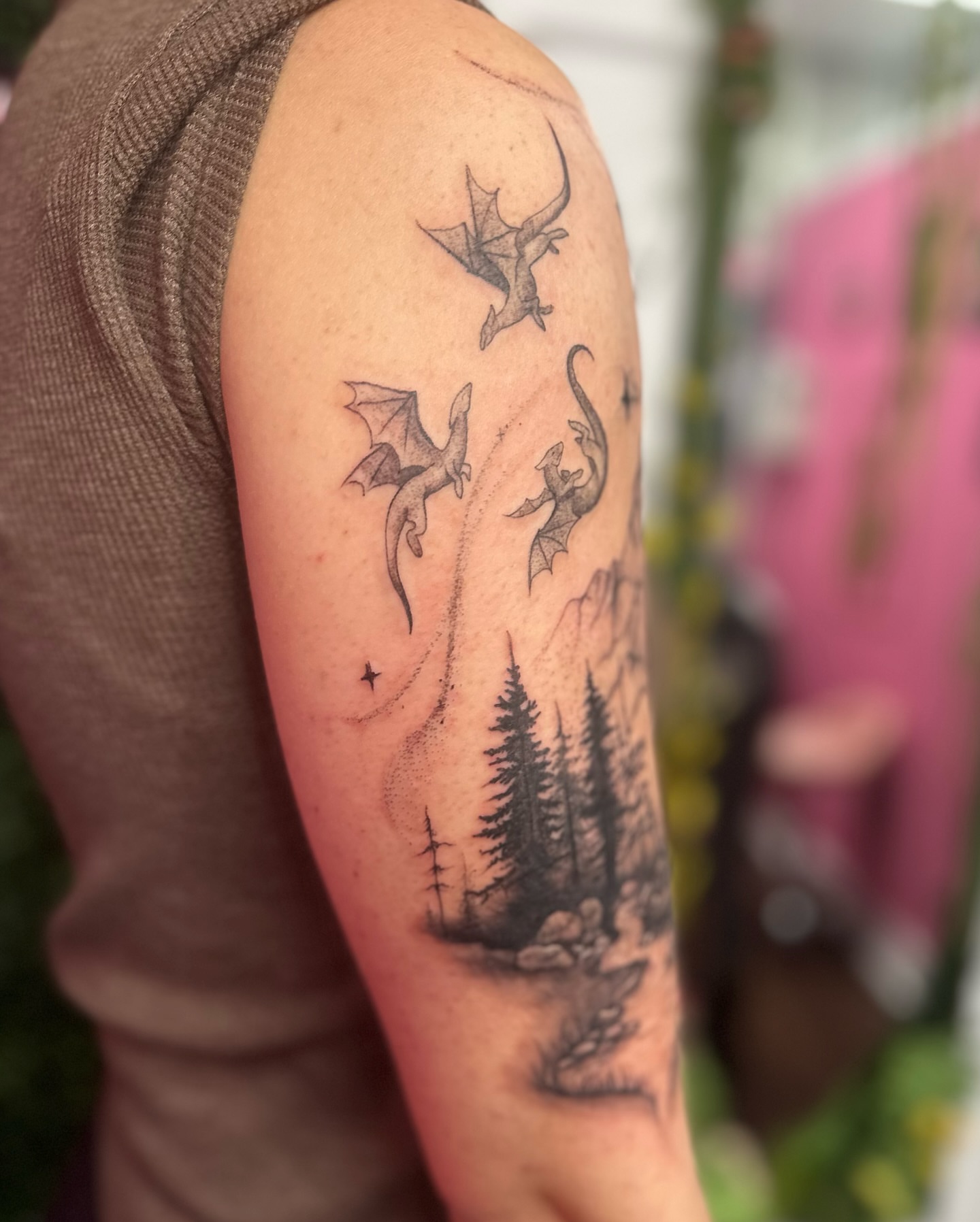 Dragons flying over forest dotwork tattoo on the upper arm by Jakki Hicks