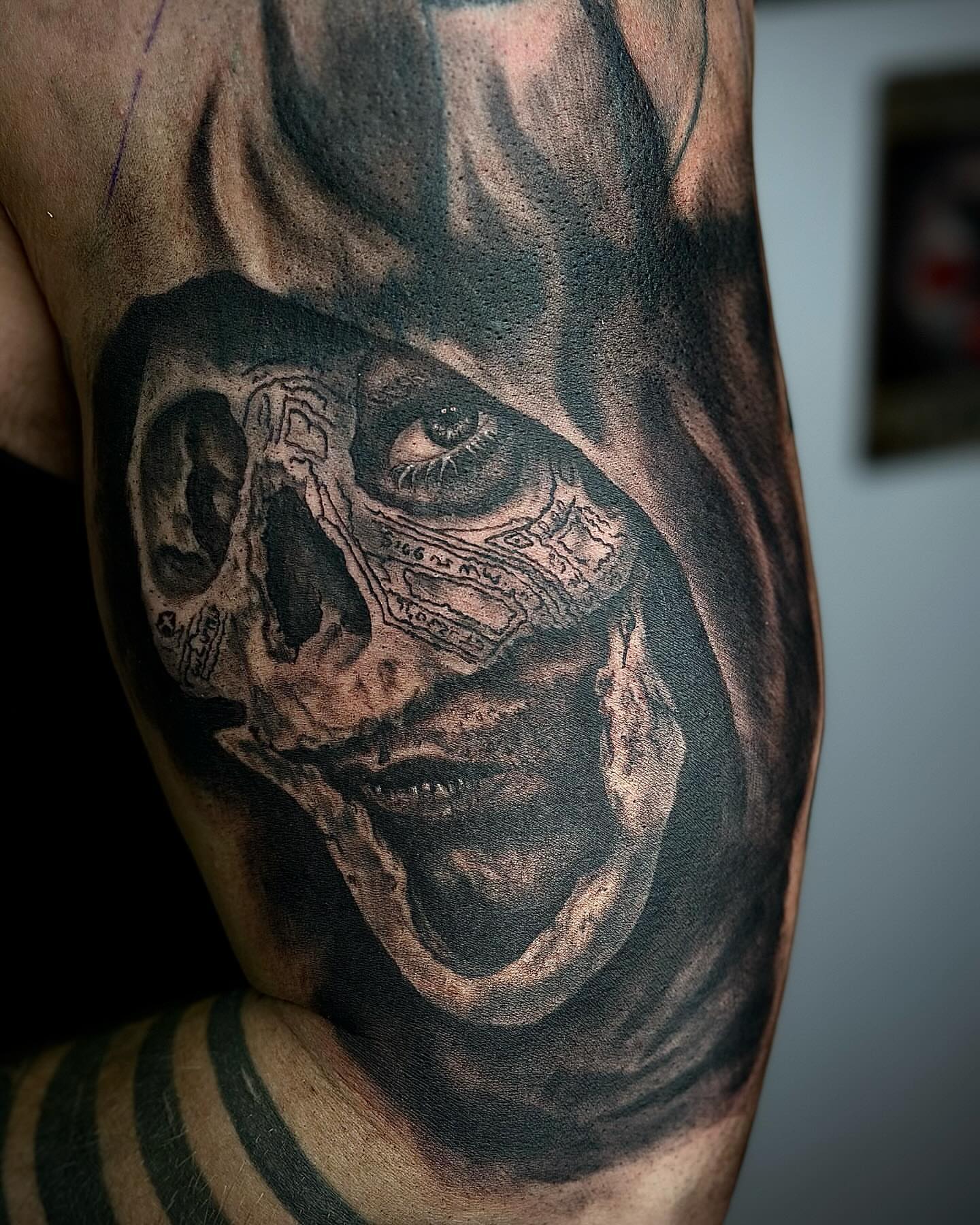Skull with mask realism tattoo on the upper arm by Brooks