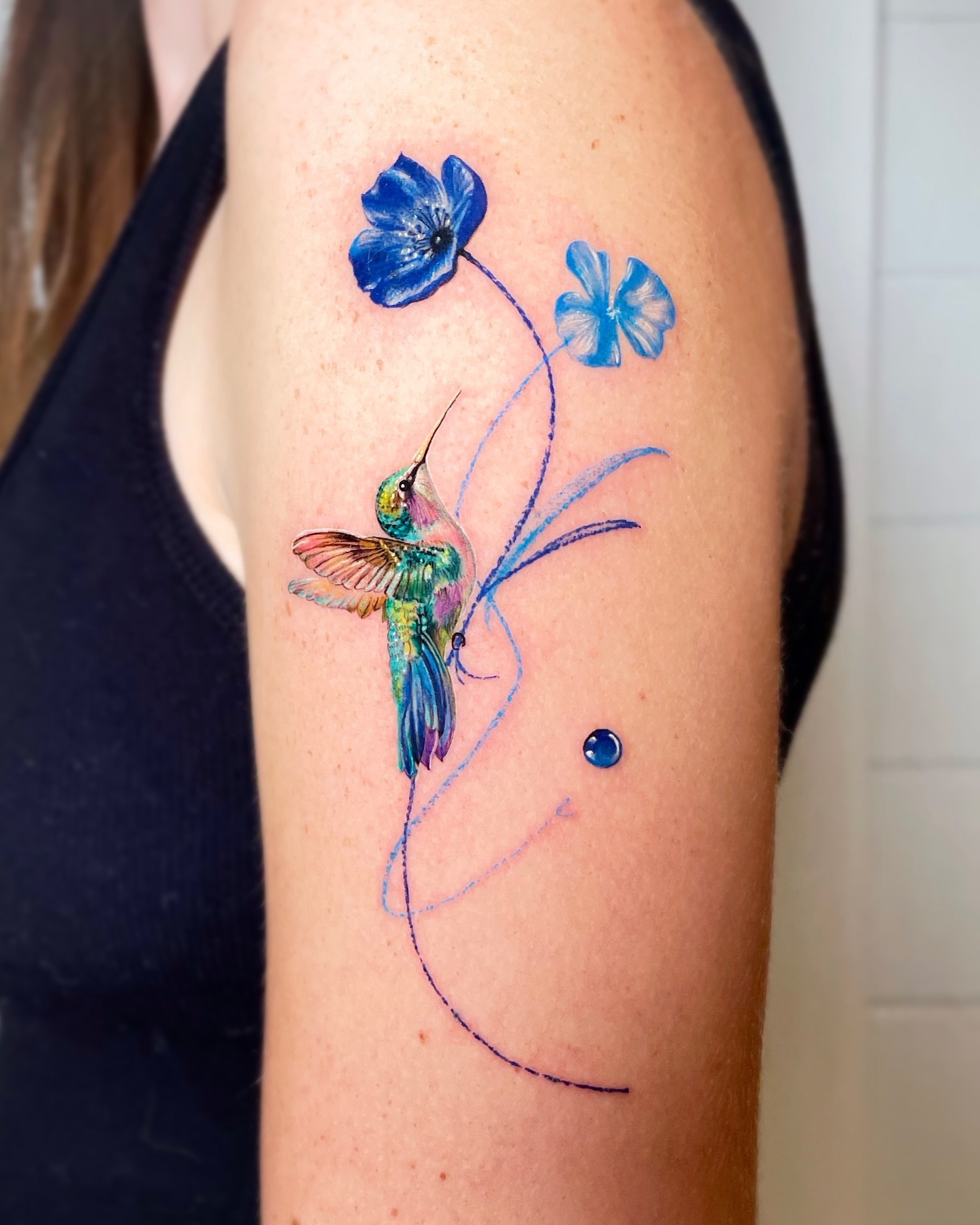 Hummingbird and flowers watercolor tattoo on the upper arm by Yeye