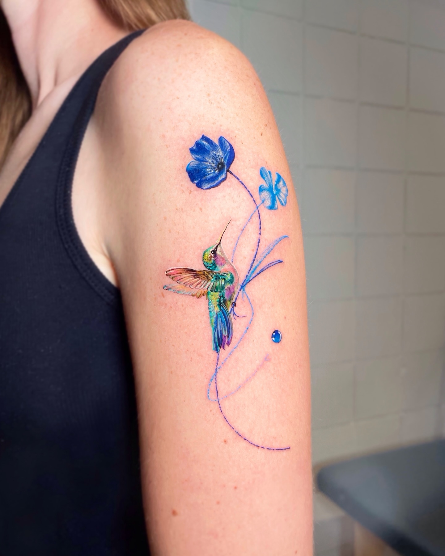 Hummingbird and flowers watercolor tattoo on the upper arm by Yeye