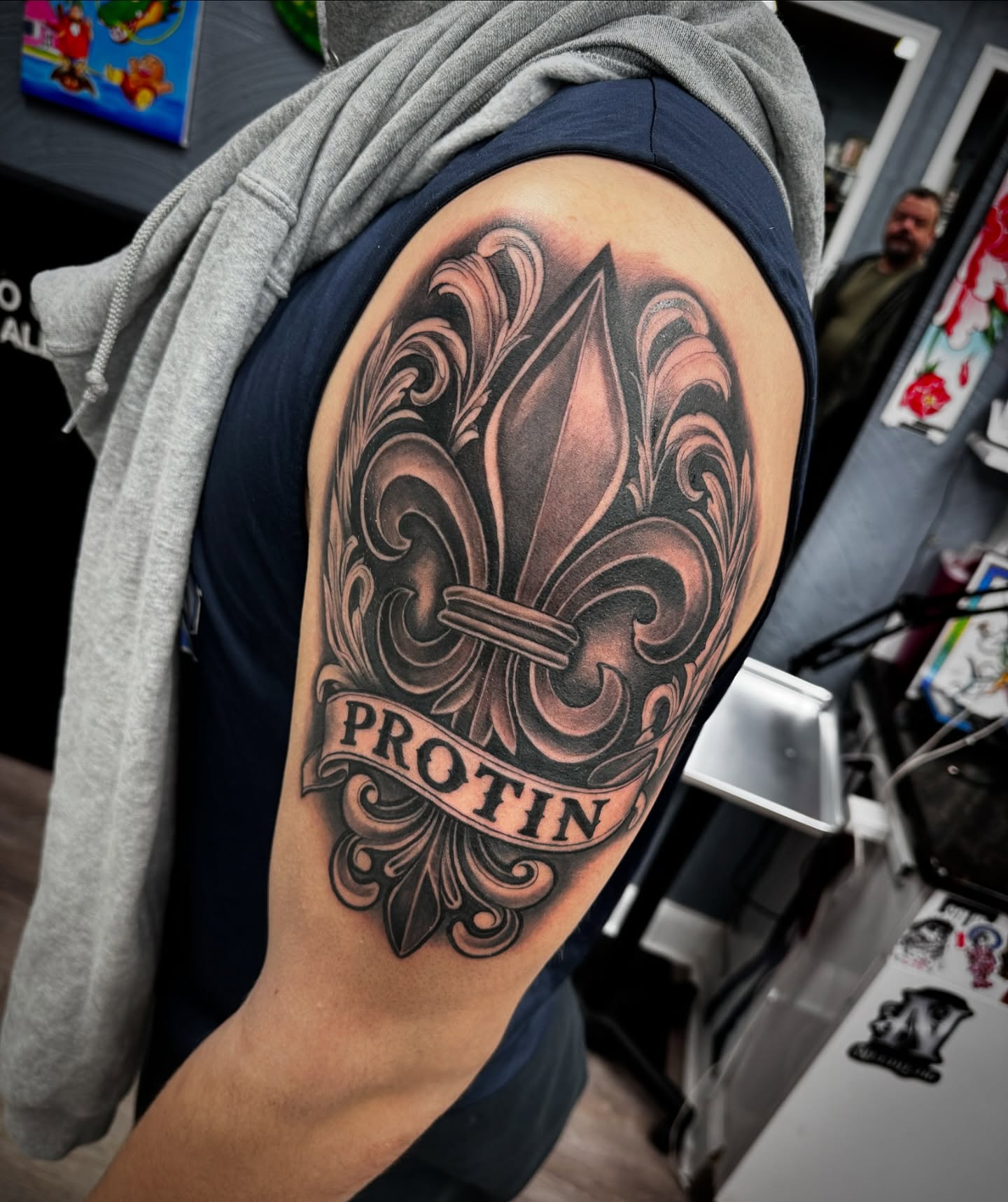 Fleur-de-lis black and grey tattoo on the upper arm by Mike Hudson