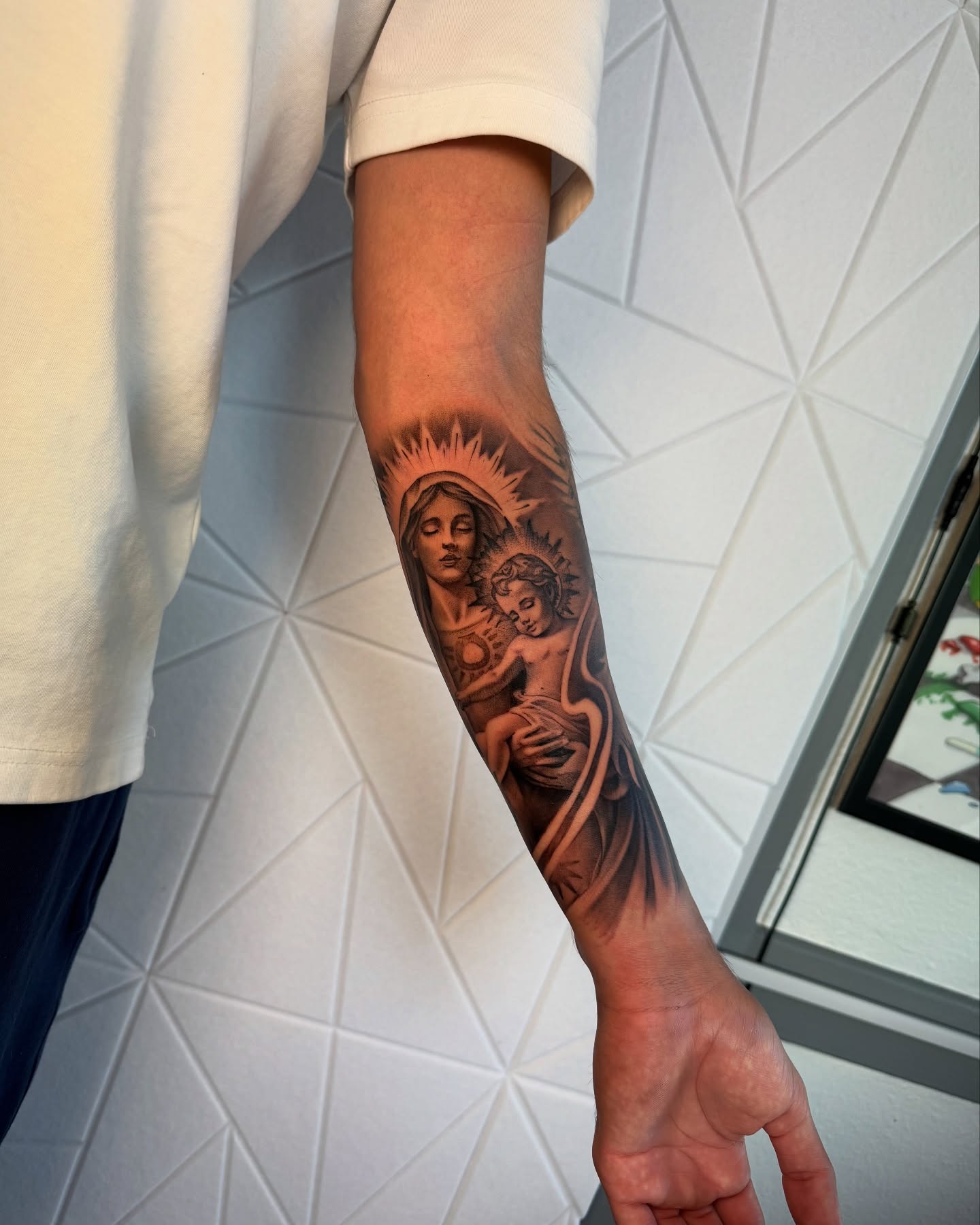 Religious figure with child black and grey tattoo on the forearm by Isiah Hall, Whittier, California