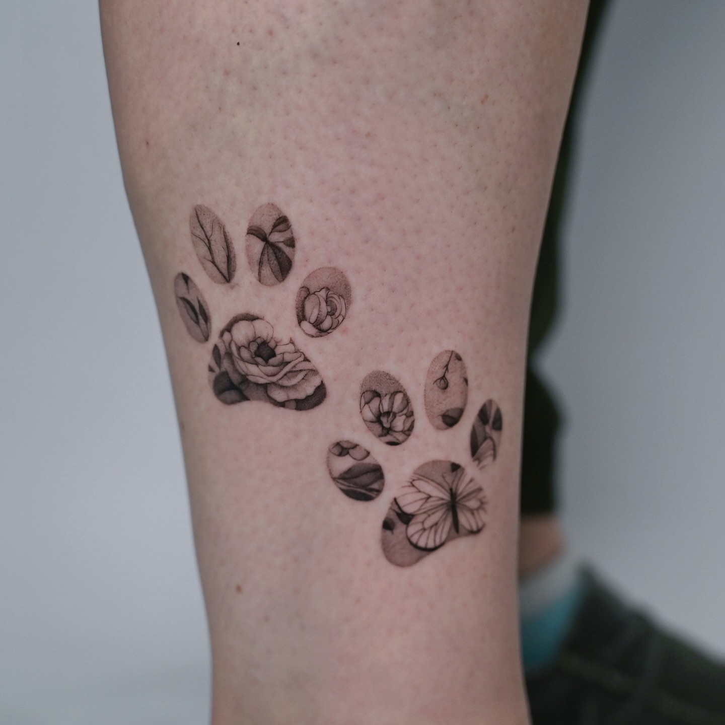 Paw prints and flowers dotwork tattoo on the forearm by dom