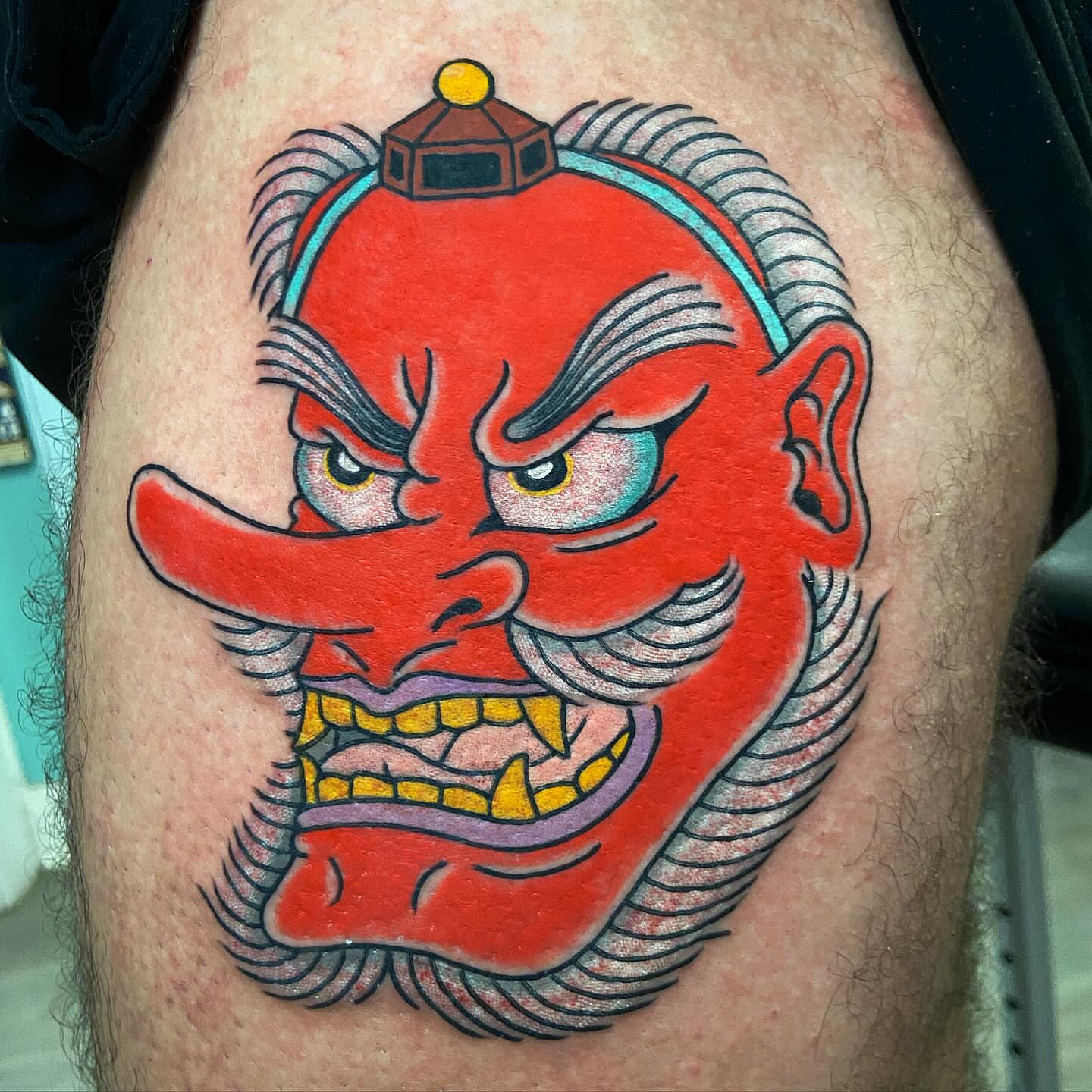 Red demon mask American traditional tattoo on the thigh by Alex Citrone - Martha’s Vineyard Tattoo