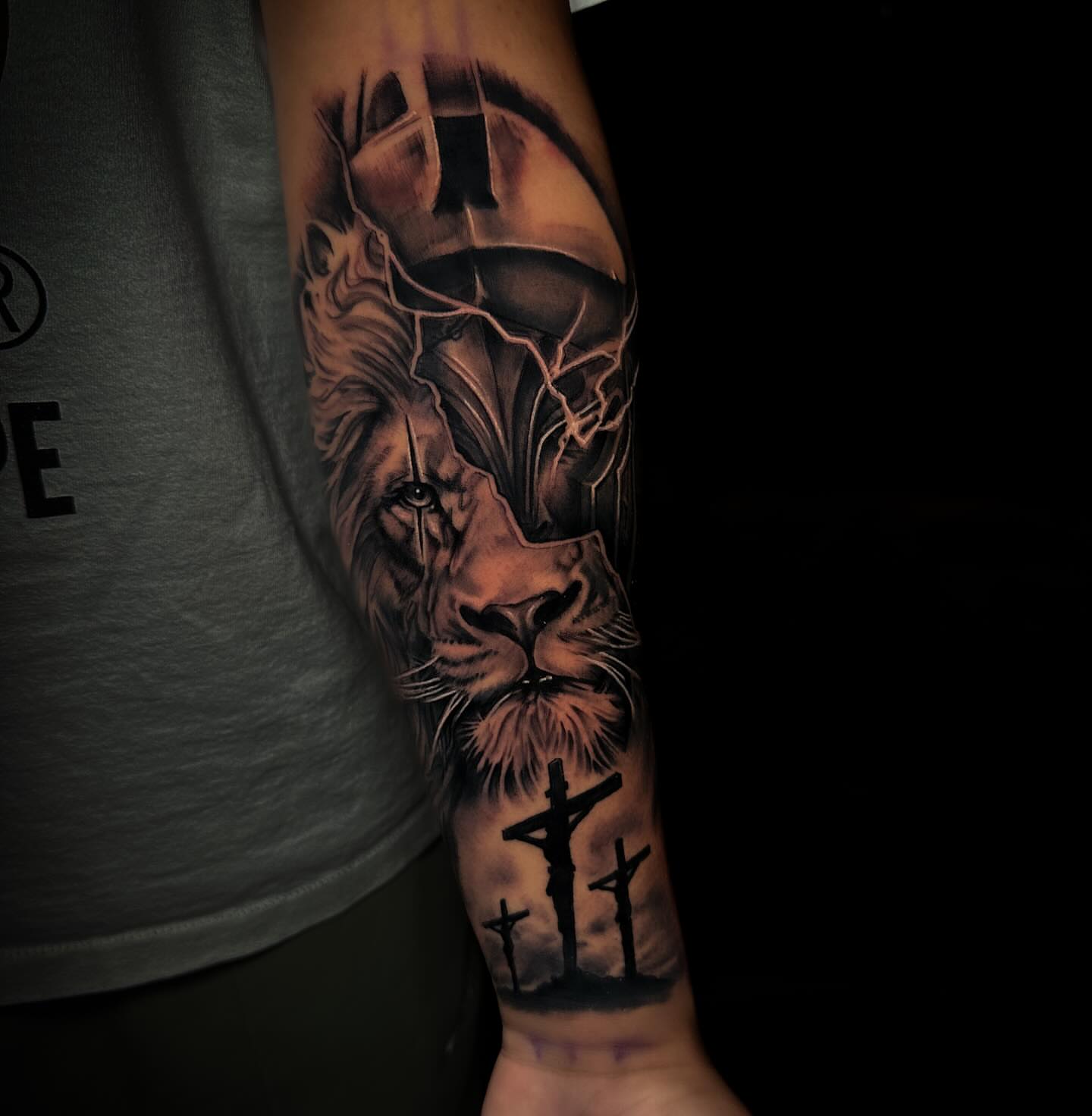 Lion and crucifixion realism tattoo on the forearm by Nick Stratt