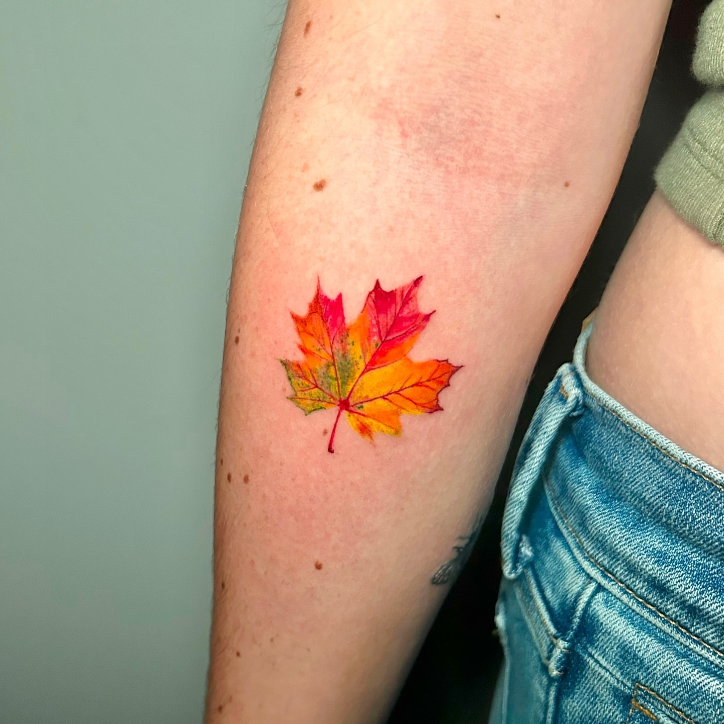 Maple leaf watercolor tattoo on the forearm by Jess