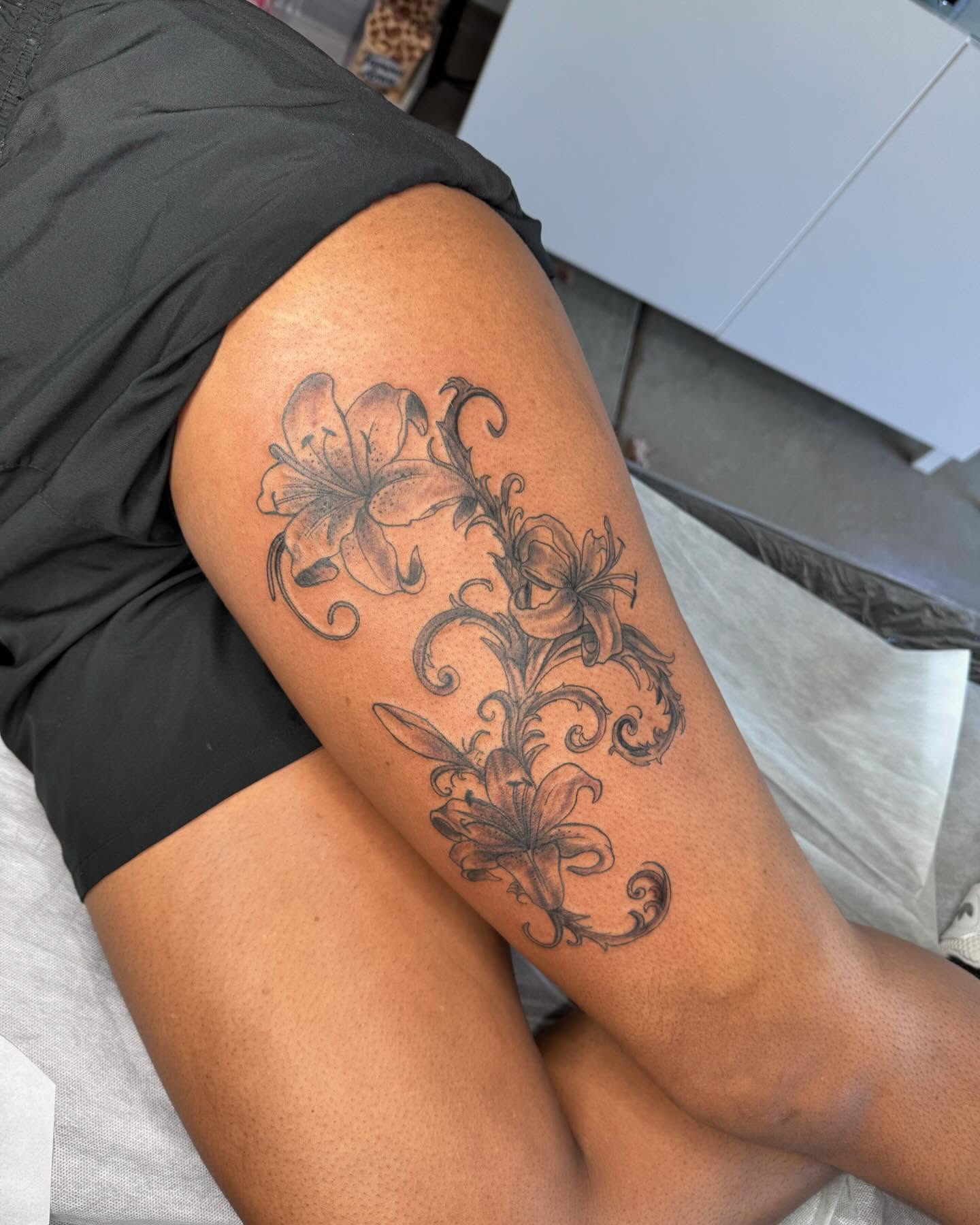 Lilies black and grey tattoo on the thigh by Sierra 🩷