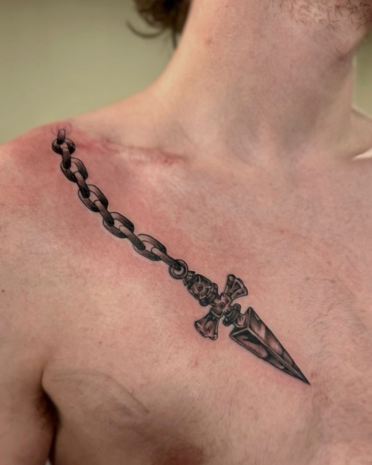 Chain and dagger black and grey tattoo on the chest by Suda