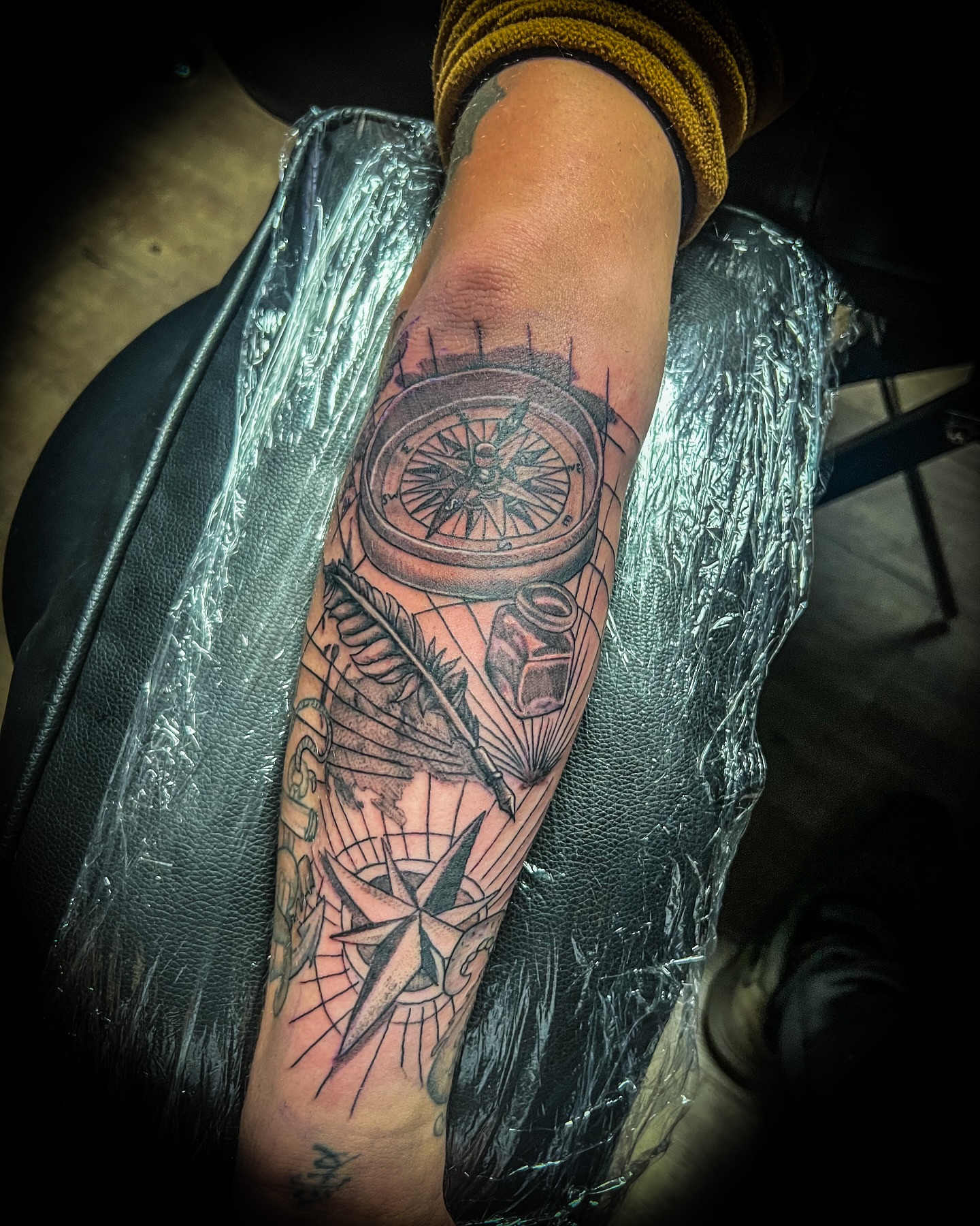 Compass and feather black and grey tattoo on the forearm by Rico Rosario