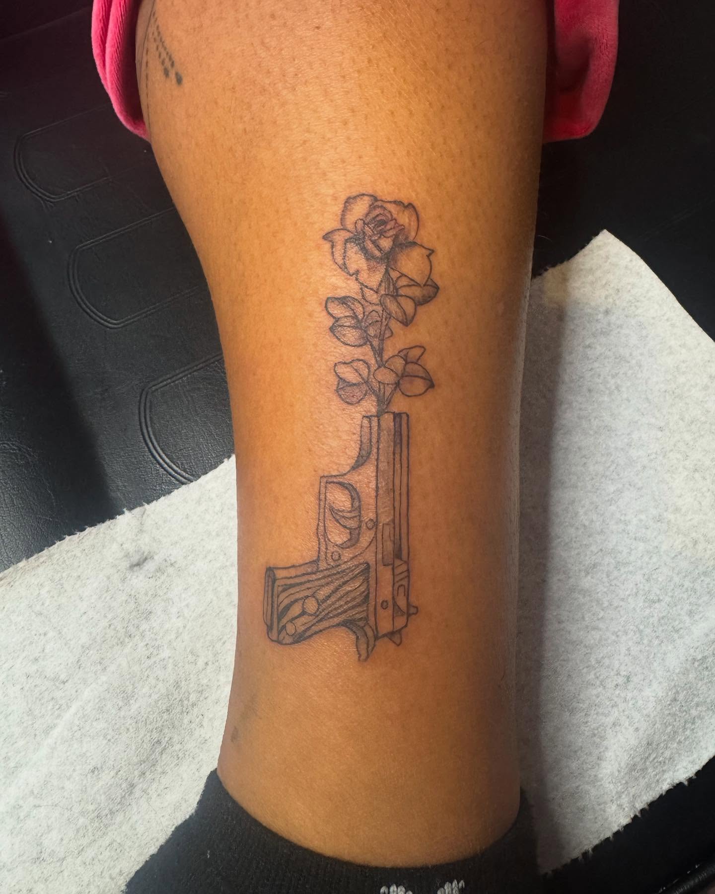 Gun with flowers black and grey tattoo on the forearm by Sonia vidal