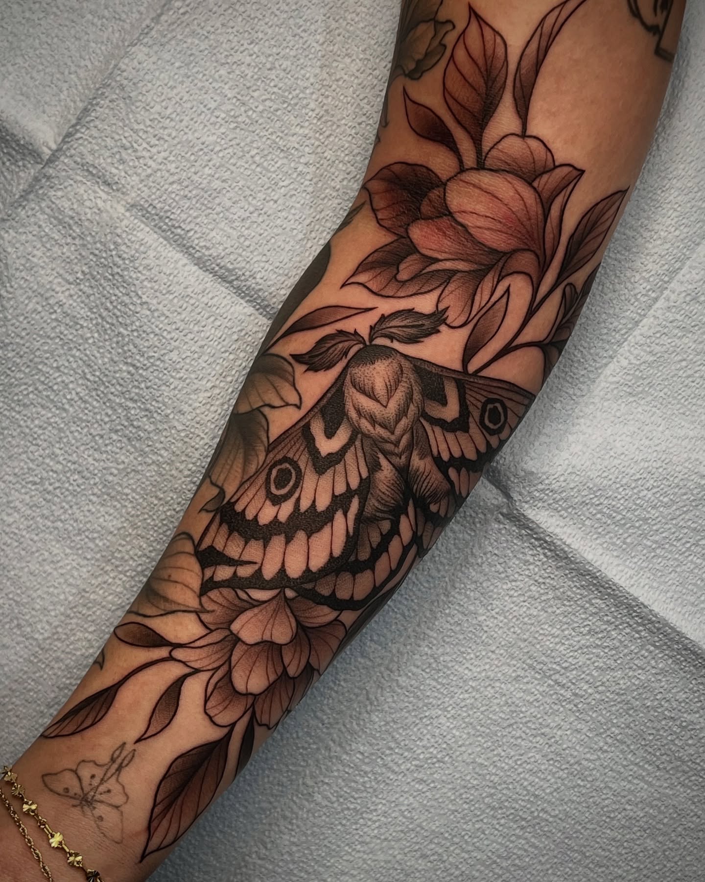 Moth and flowers black and grey tattoo on the forearm by Mia Manzanedo