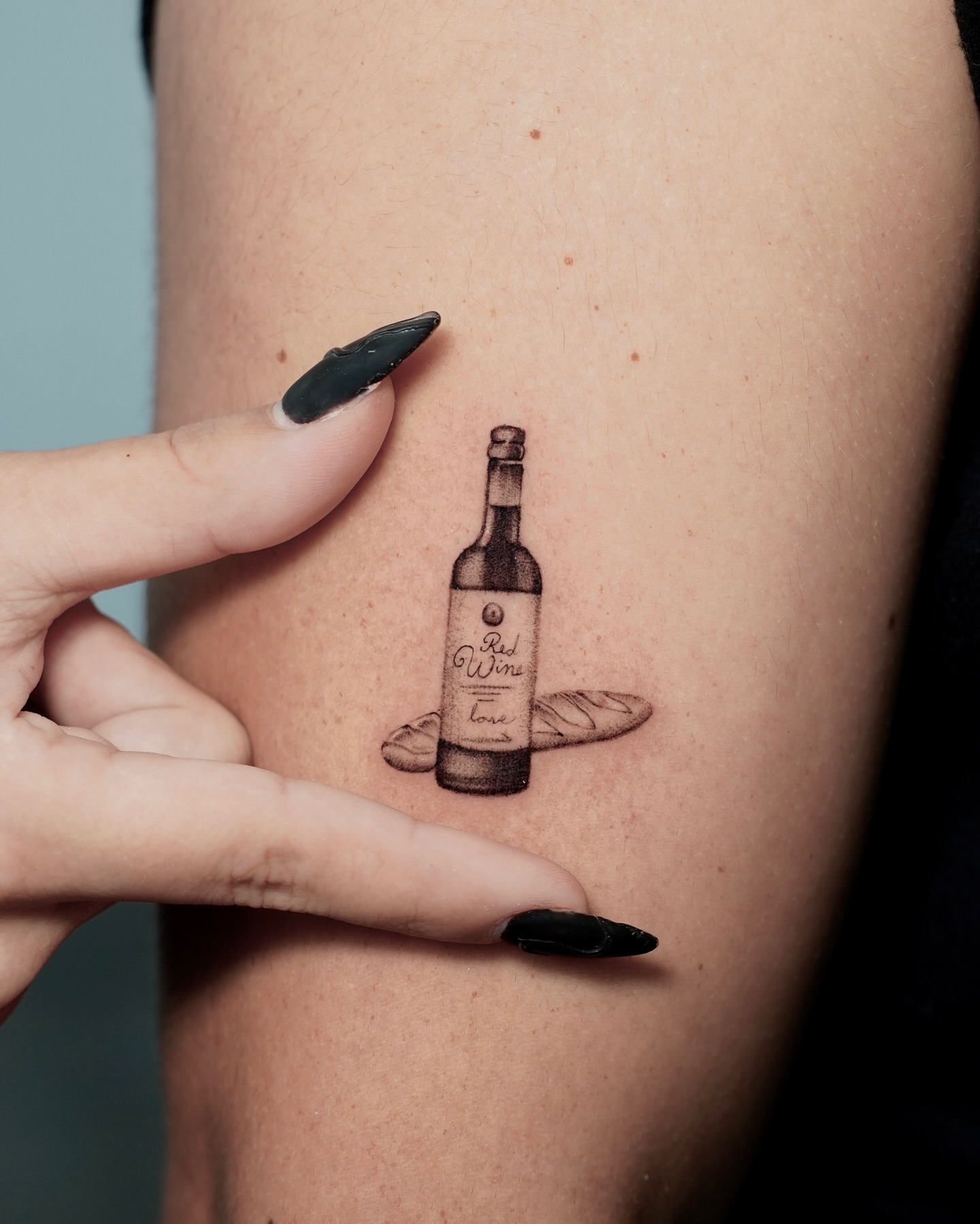Wine bottle black and grey tattoo on the forearm by Sophia Delfino