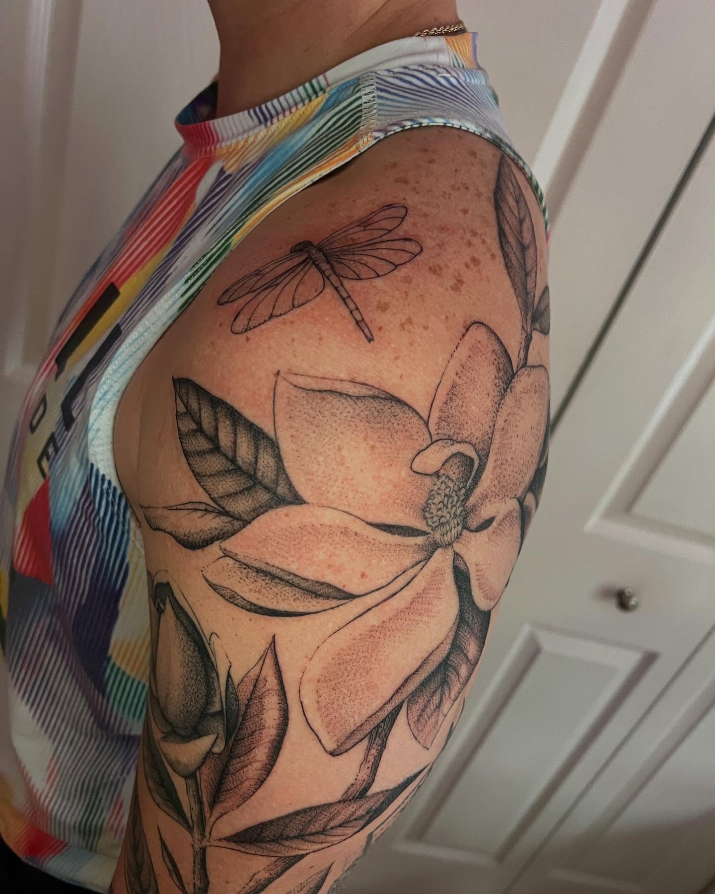 Magnolia flower and dragonfly realism tattoo on the upper arm by Natasha