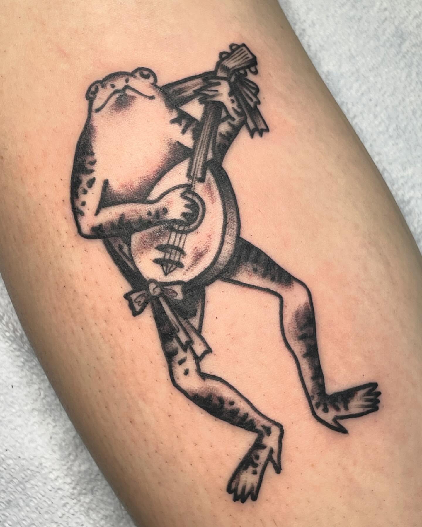 Frog playing banjo black and grey tattoo on the thigh by G. Clover ⚧︎, Chicago, Illinois
