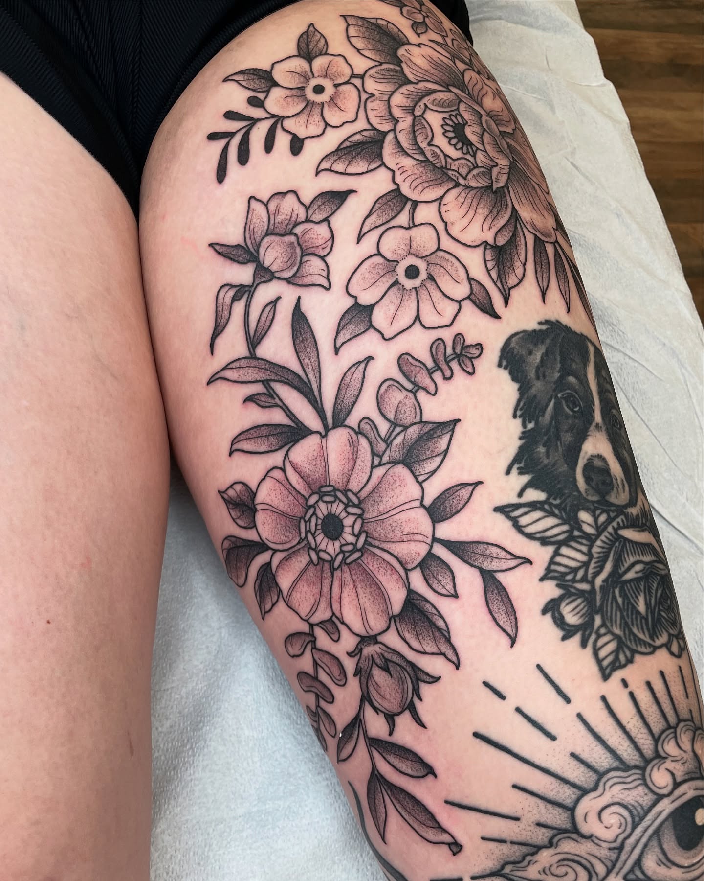 Floral bouquet with dog black and grey tattoo on the thigh by Emily Lux