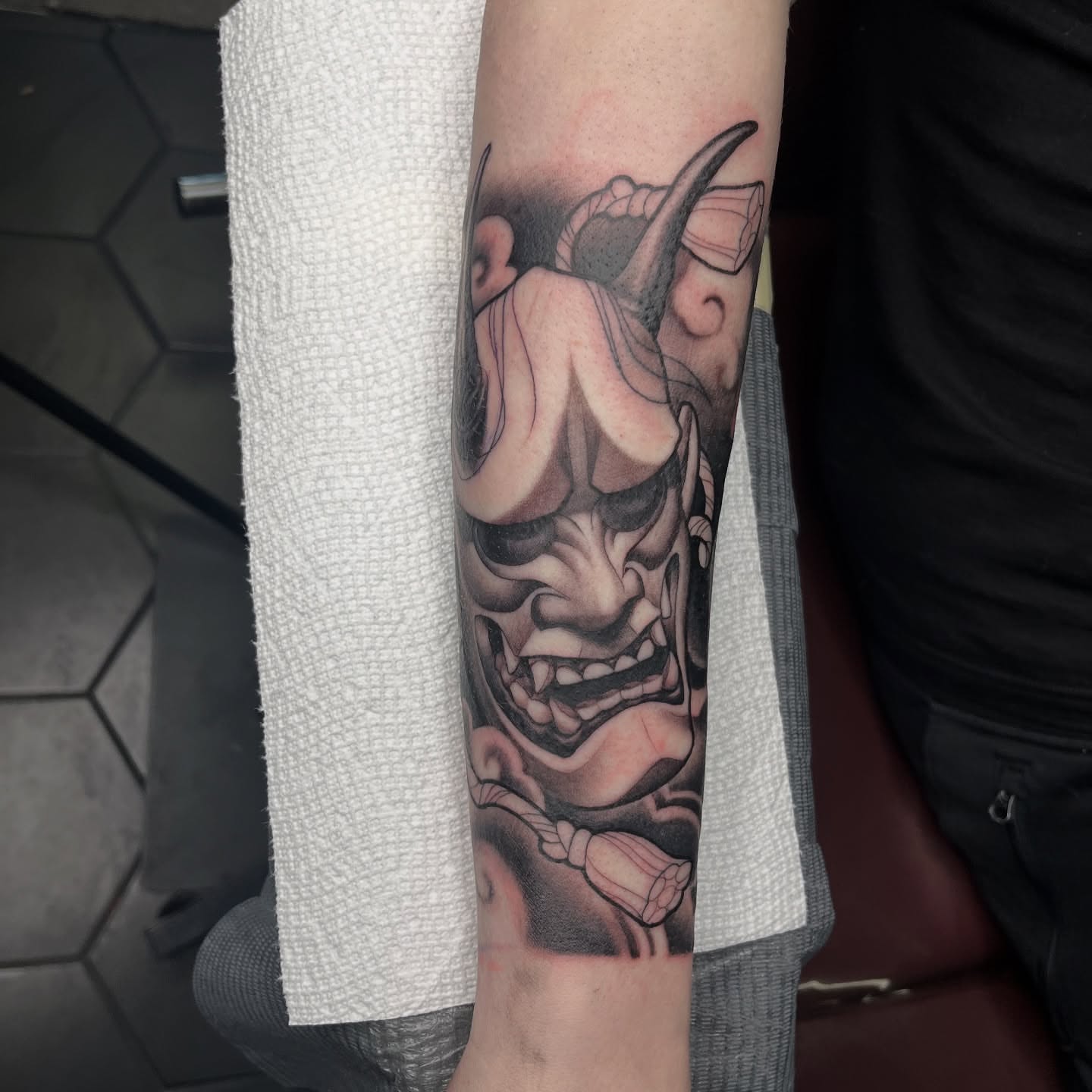 Demon mask black and grey tattoo on the forearm by Angelique Sanders, Tellico Plains, Tennessee