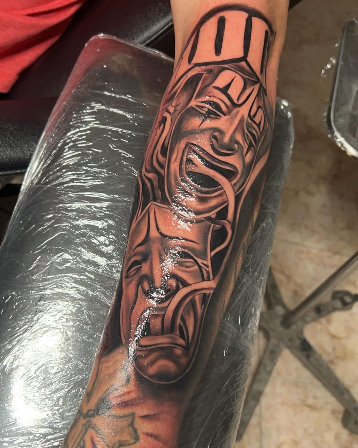 Theatrical masks realism tattoo on the forearm by Bryant Ramirez