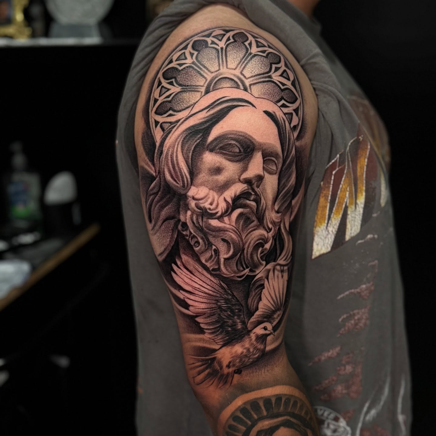 Religious figure with dove realism tattoo on the upper arm by Carlos Lujan