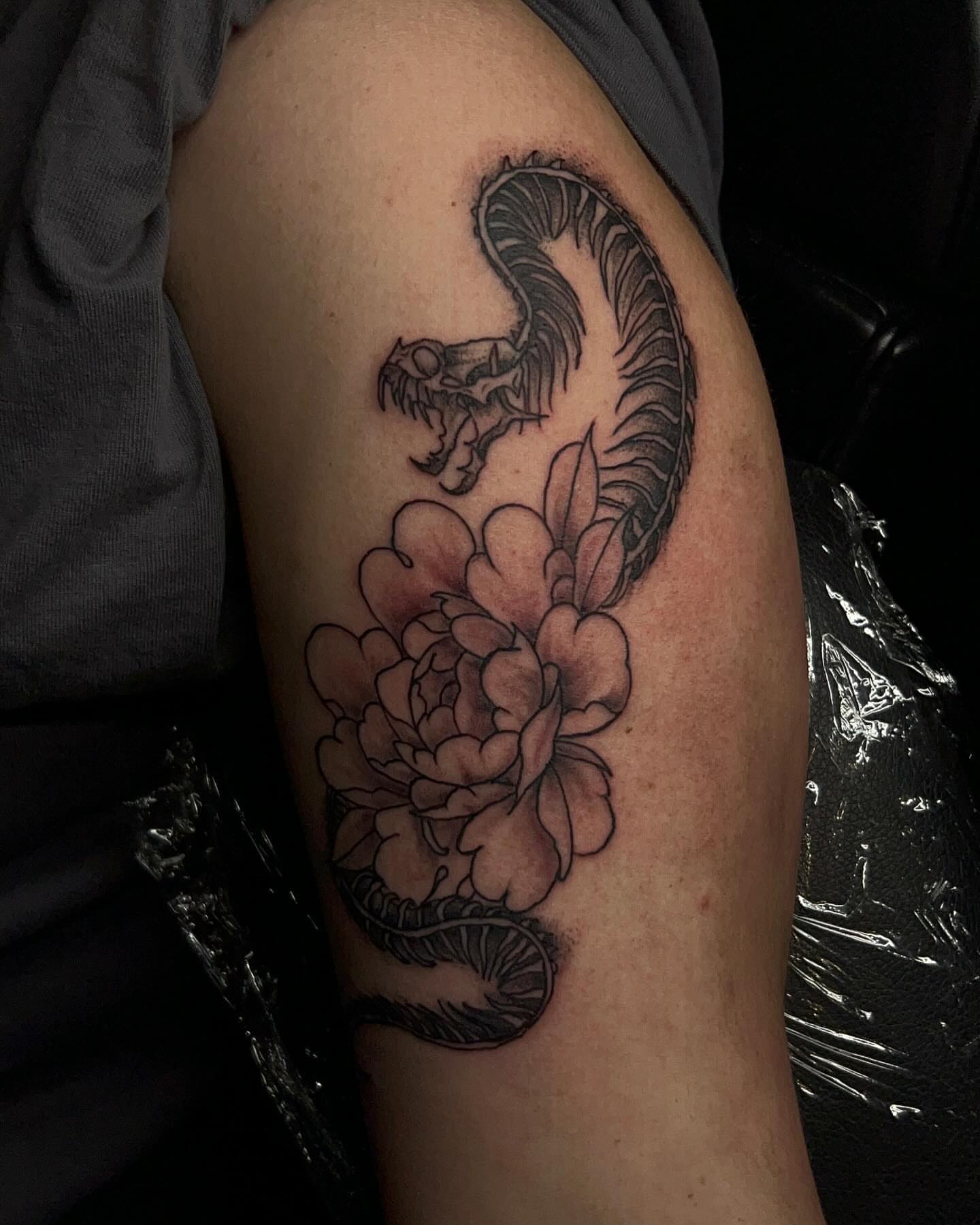 Snake and peony black and grey tattoo on the upper arm by Joey-tattoo Artist