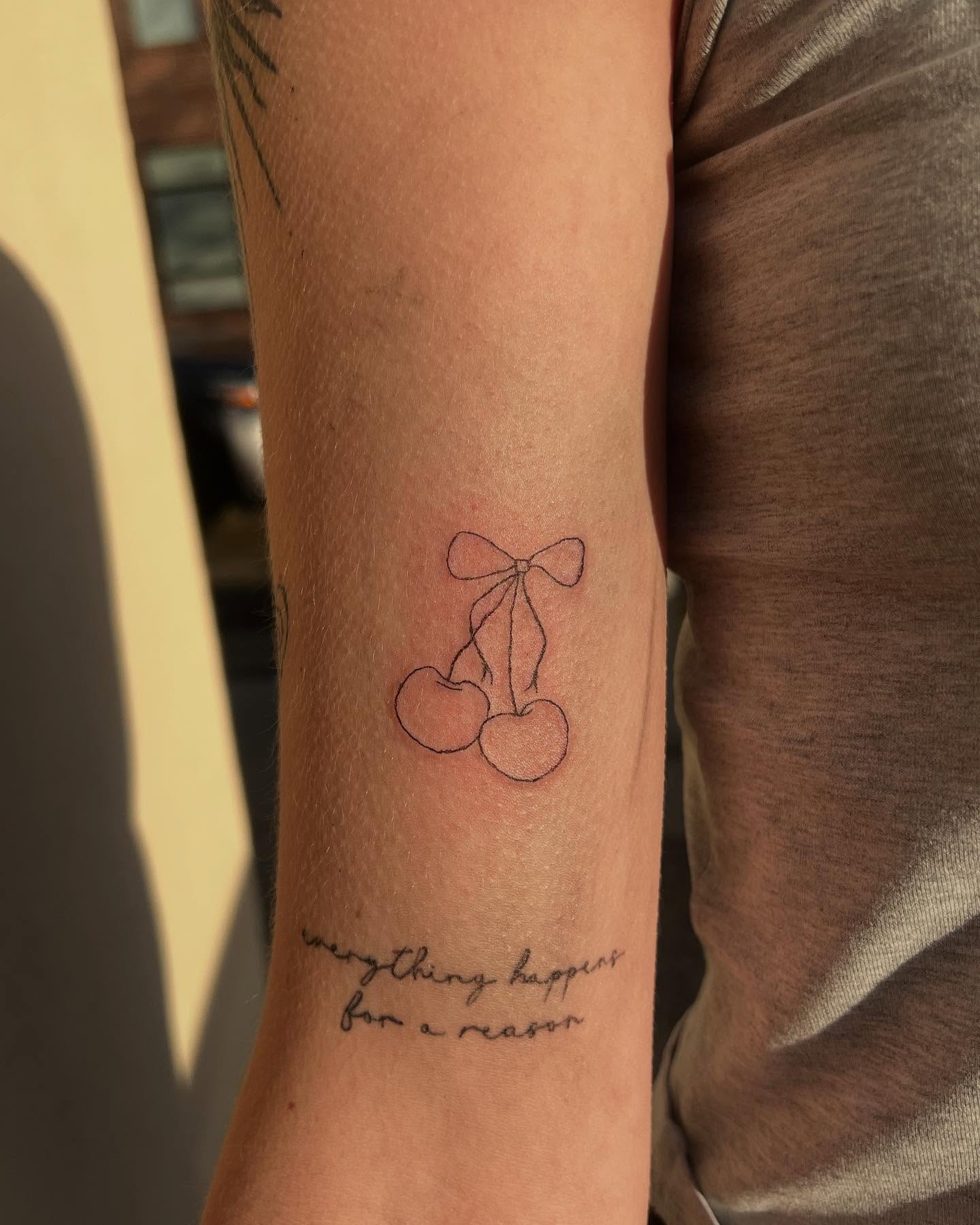 Cherry with bow fine line tattoo on the forearm by Kylee Snow
