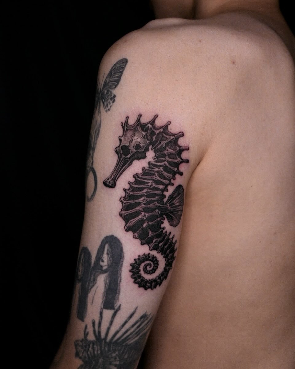 Seahorse black and grey tattoo on the upper arm by 𝑴𝒆𝒍𝒐
