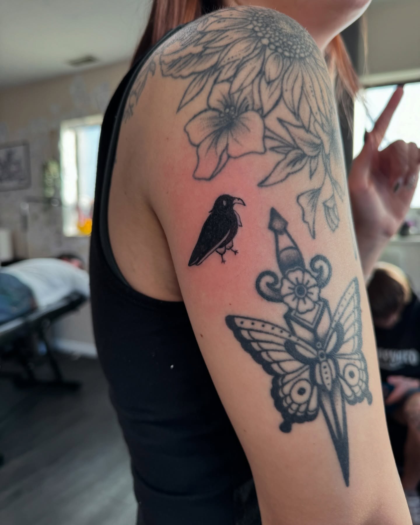 Bird, butterfly, flowers black and grey tattoo on the upper arm by @inkspirationtattoo_co