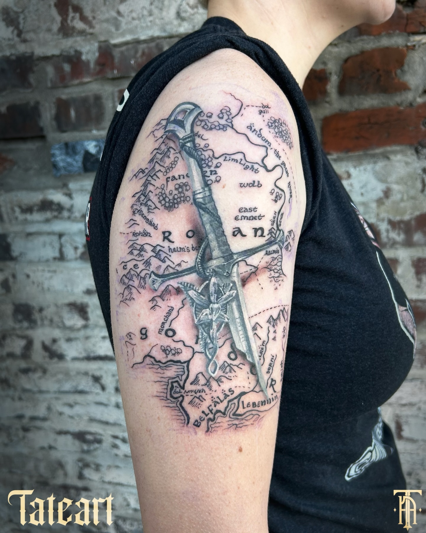 Map with sword black and grey tattoo on the upper arm by Tate Wortham