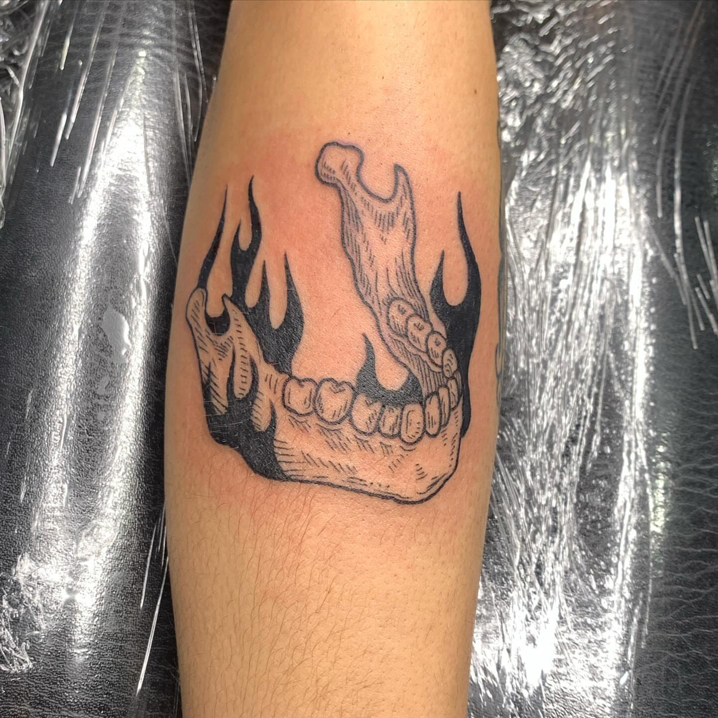 Flaming jawbone black and grey tattoo on the forearm by Ava Glory Tattoos