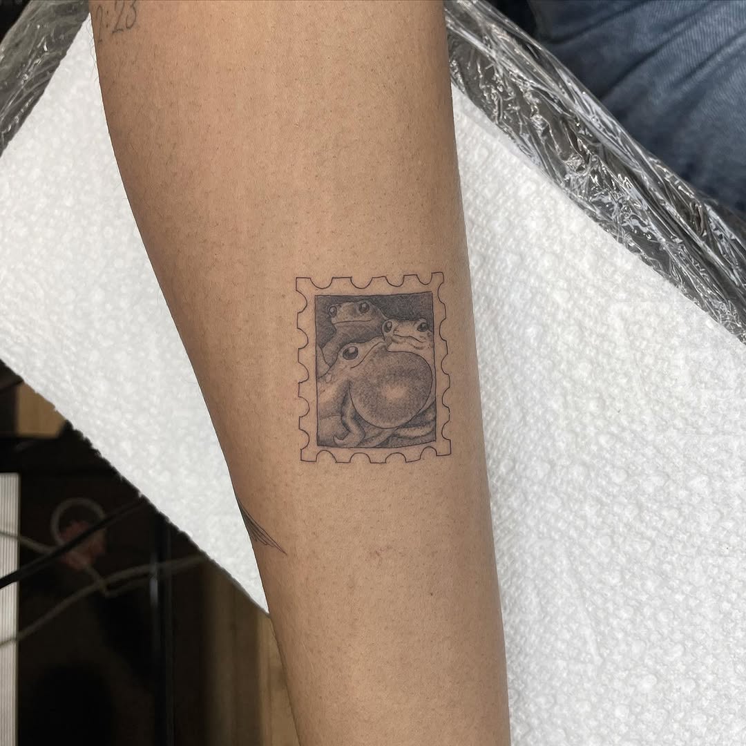 Frogs on a stamp minimalist tattoo on the forearm by Jesus A.