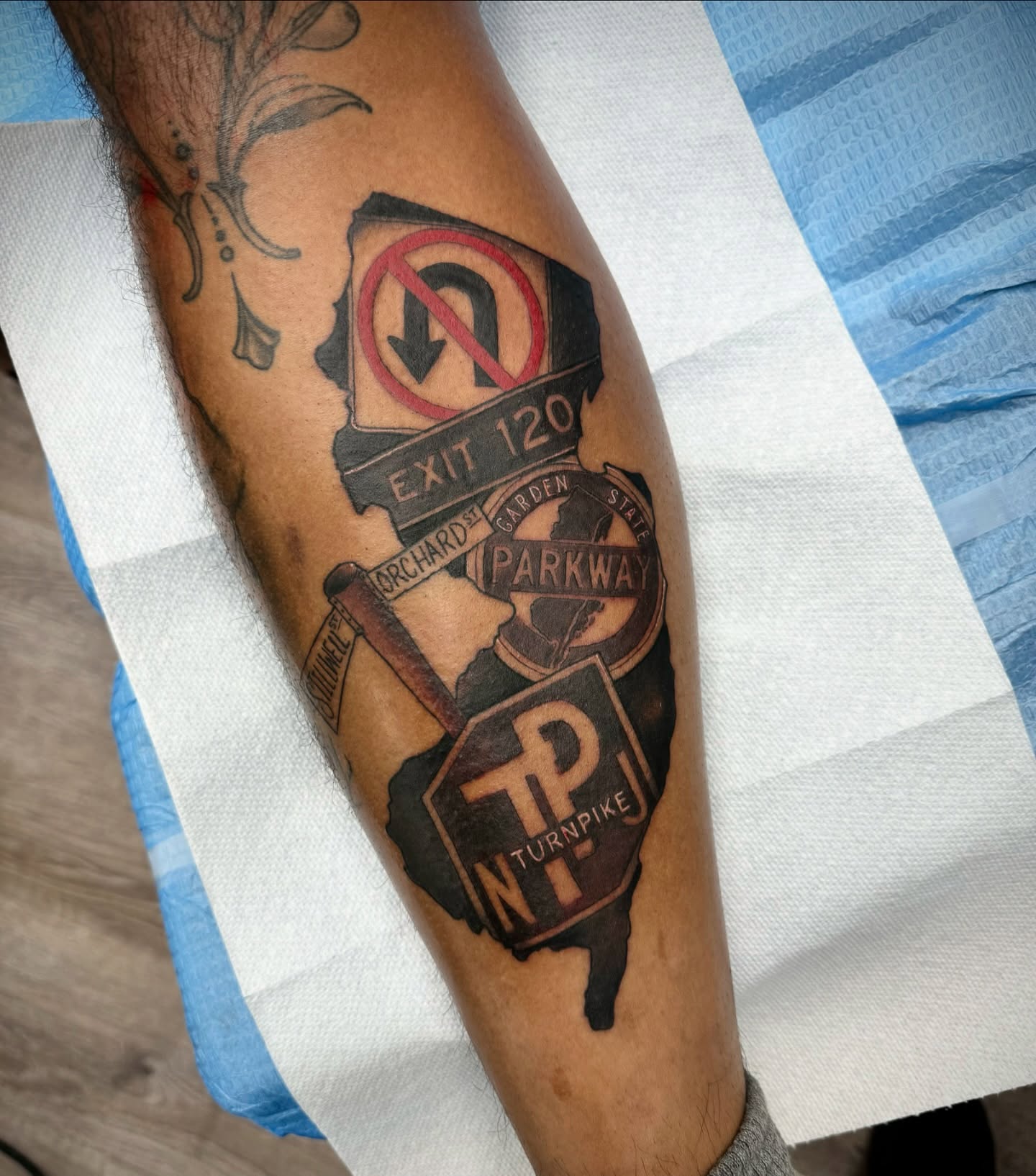 Road signs black and grey tattoo on the forearm by Mike Hudson