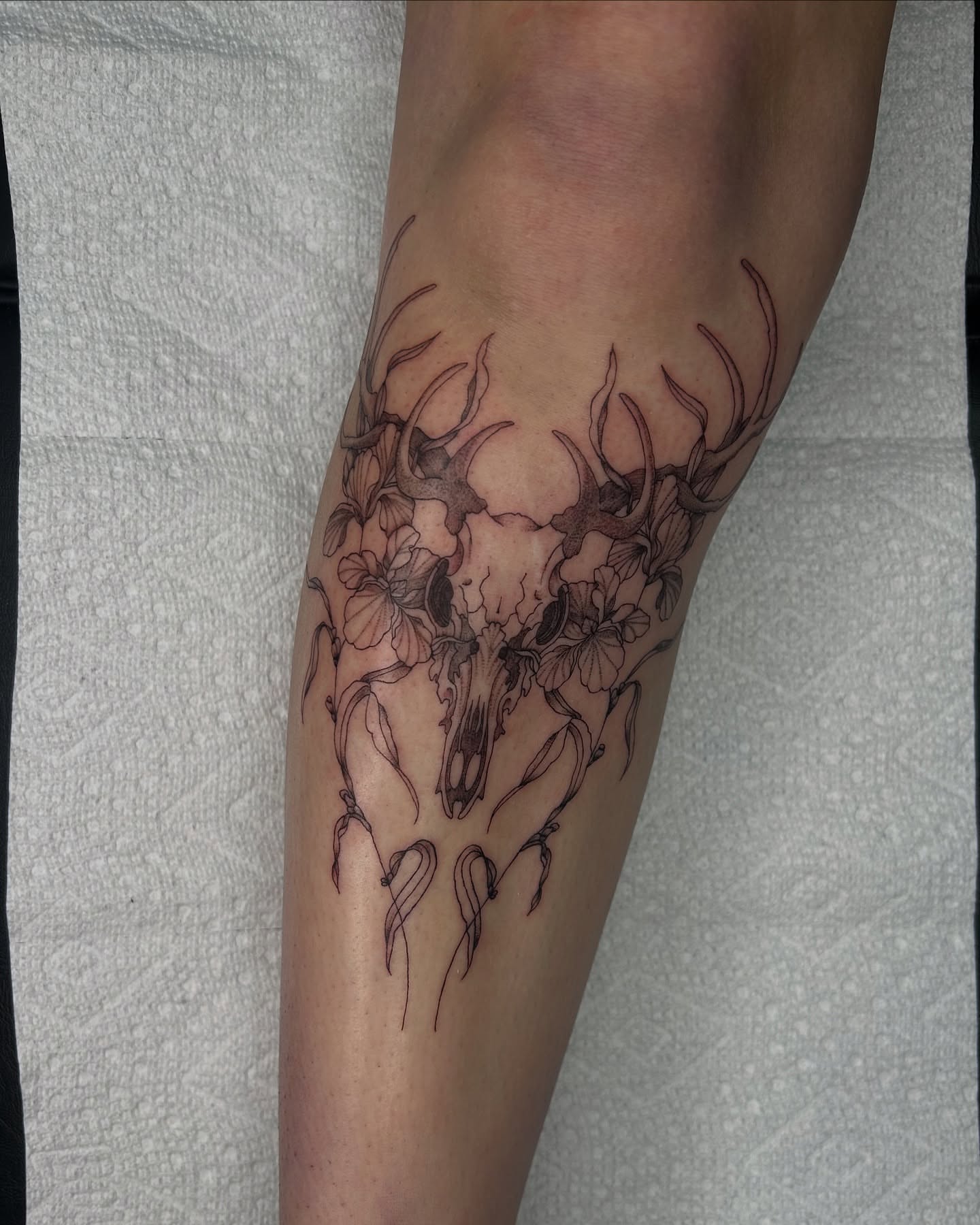 Deer skull with flowers black and grey tattoo on the forearm by Kennedy Ramey